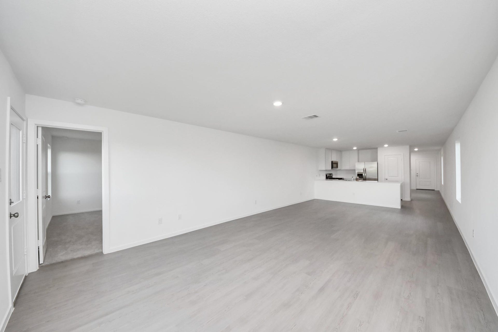 3096 Sunset Glory Drive, Katy, TX 77493 This photo showcases a spacious, open-concept living area with light wood flooring and a modern kitchen featuring stainless steel appliances. The room is bright with ample lighting and neutral walls, providing a versatile space for customization.