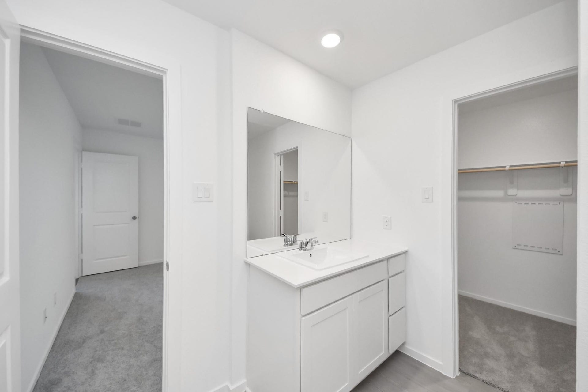 3096 Sunset Glory Drive, Katy, TX 77493 This photo features a bright, modern bathroom with a single vanity, large mirror, and ample storage. It connects to a carpeted hallway and a walk-in closet, offering convenience and functionality.