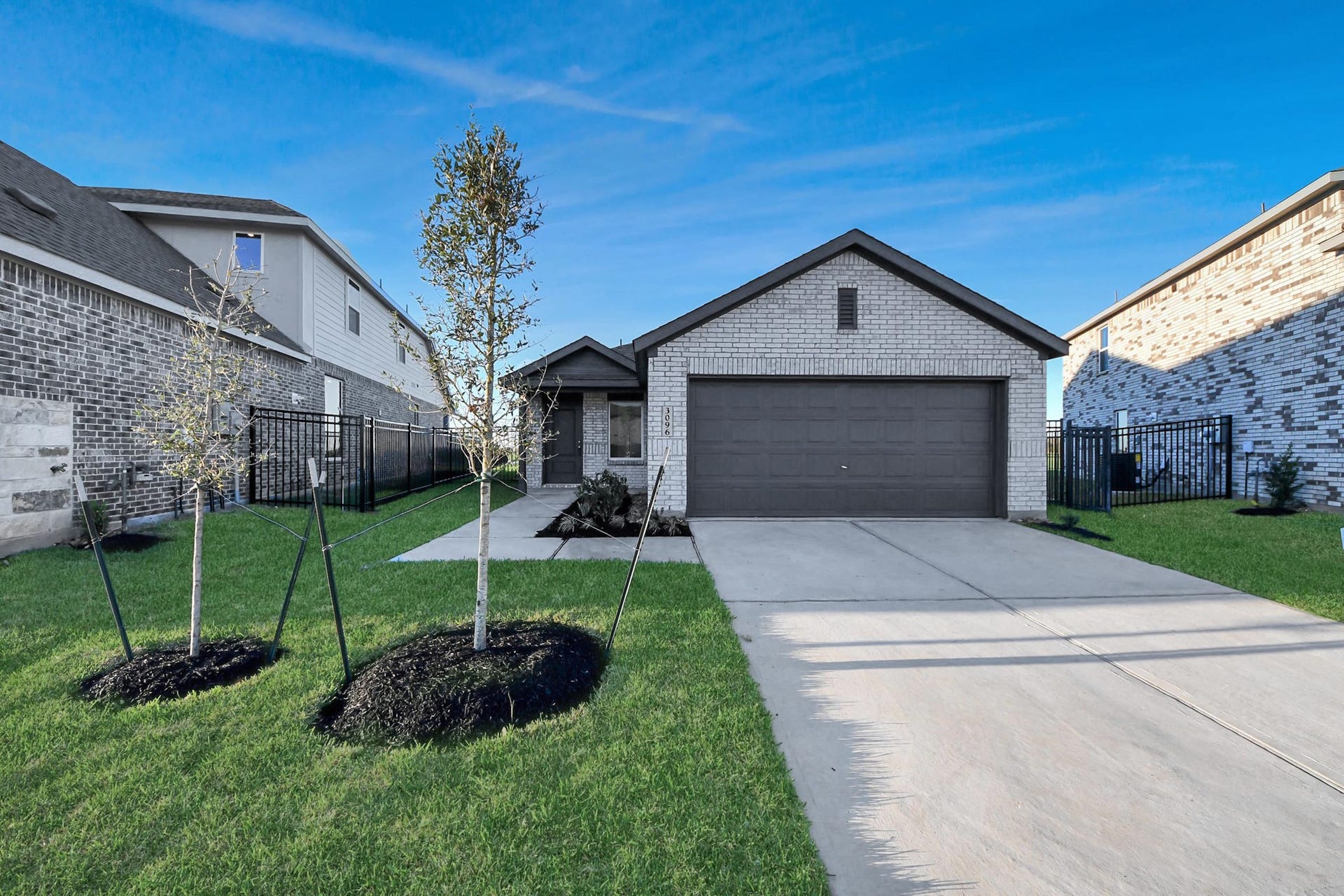 3096 Sunset Glory Drive, Katy, TX 77493 This photo showcases a modern single-story brick home with a two-car garage. It features a neatly landscaped front yard with young trees and a wide driveway. The exterior has a clean, contemporary look, ideal for a family home.