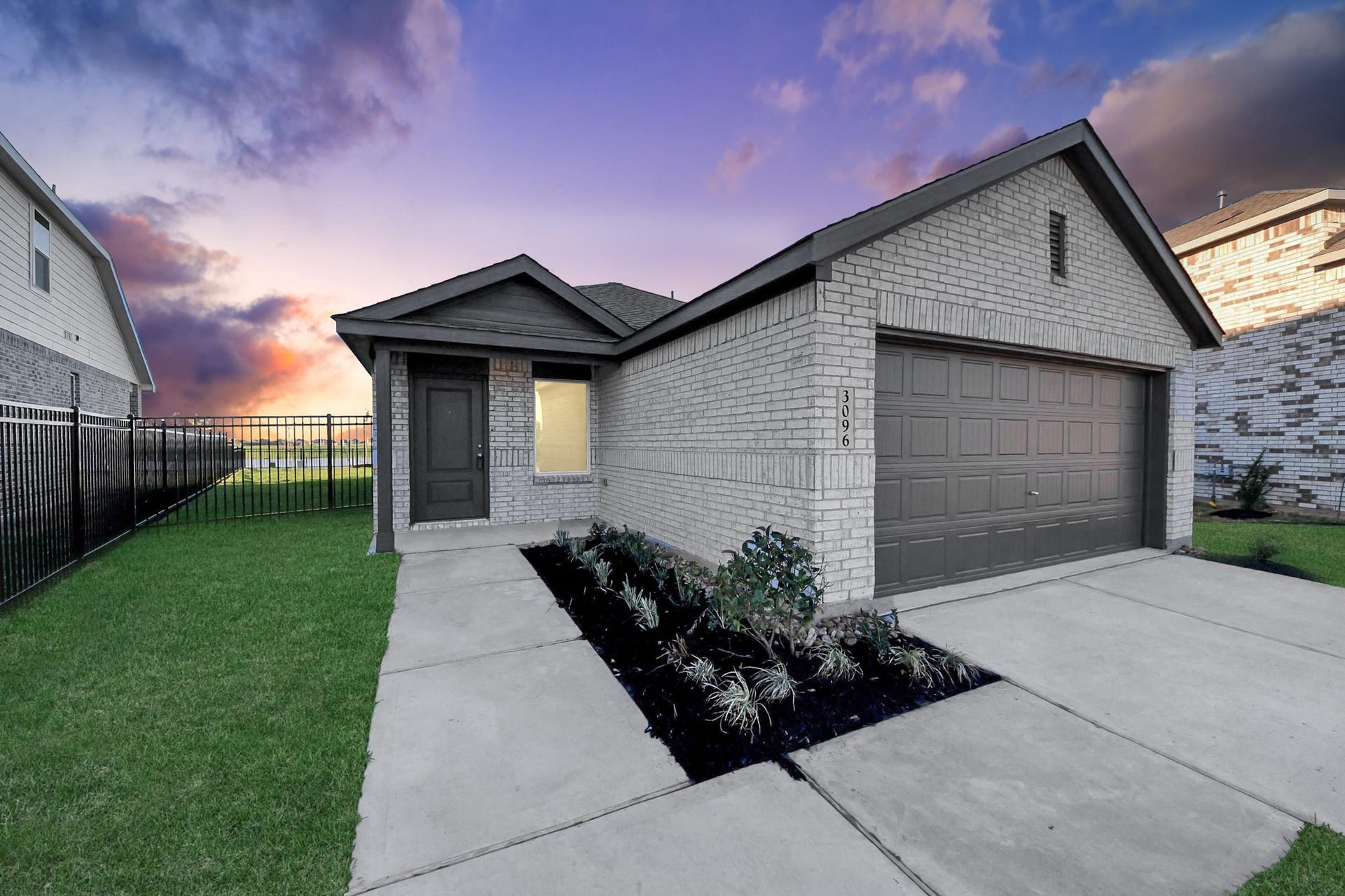 3096 Sunset Glory Drive, Katy, TX 77493 This photo features a modern, single-story brick home with a clean, well-maintained exterior. It includes a two-car garage, a small front garden, and a spacious driveway. The setting sun in the background adds a warm, inviting ambiance.