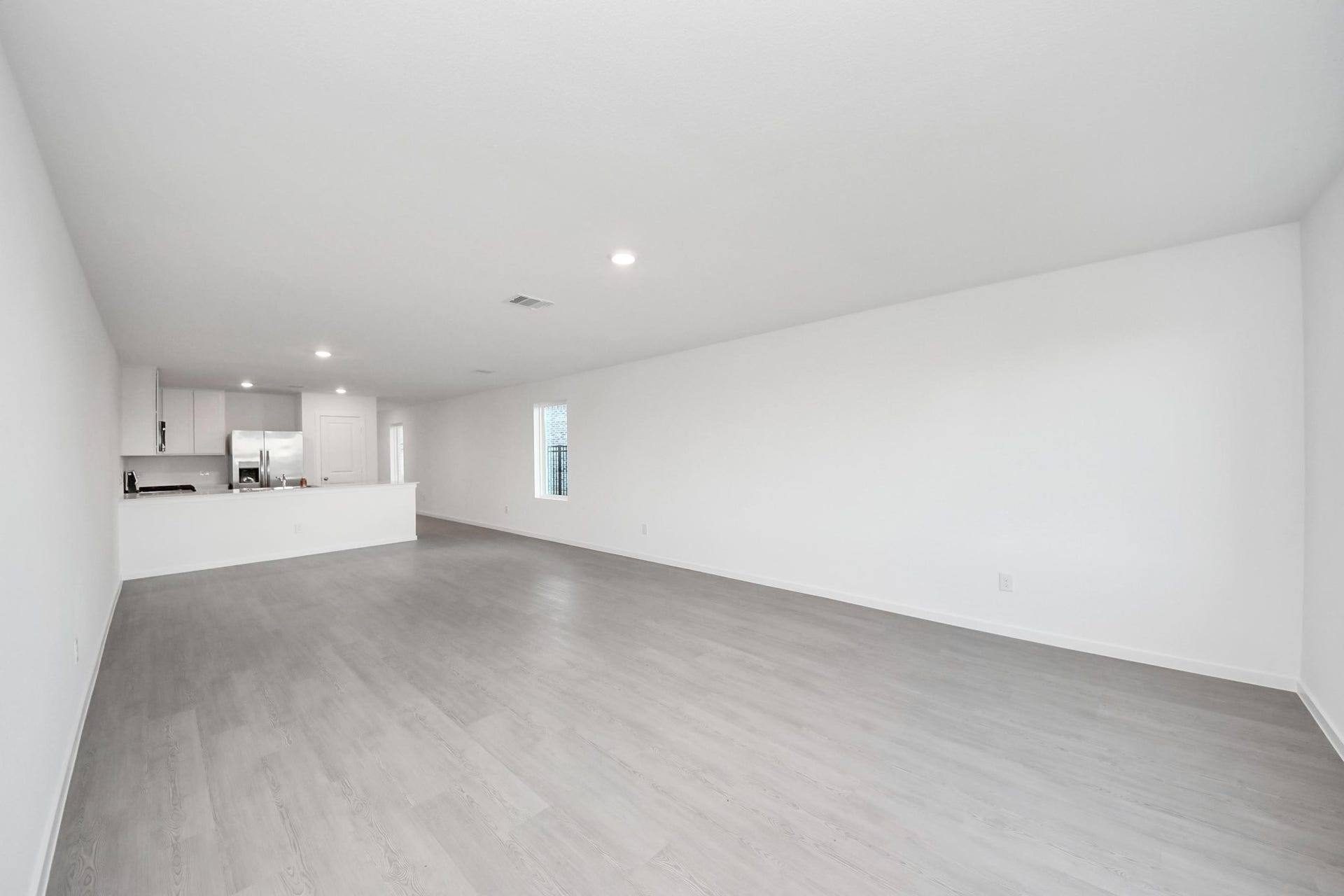 3096 Sunset Glory Drive, Katy, TX 77493 This photo showcases a spacious, open-concept living area with light gray flooring and white walls. The room flows into a modern kitchen with stainless steel appliances and a large counter, offering ample space for dining and entertaining.