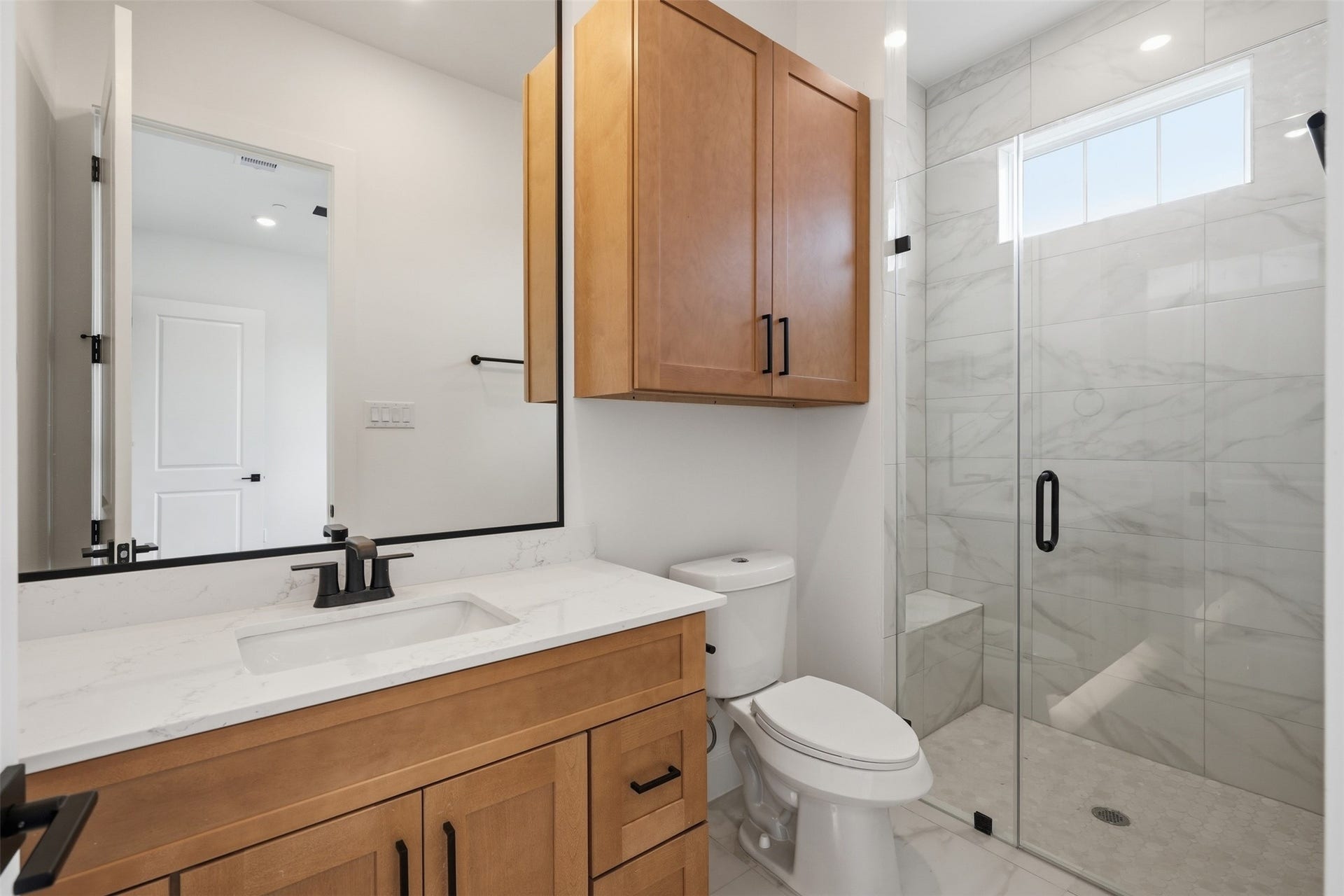 2111 Nantucket Drive, #C, Houston, TX 77057 The secondary en-suite bath features a walk-in shower, warm wood cabinetry, quartz countertops, and sleek black fixtures.