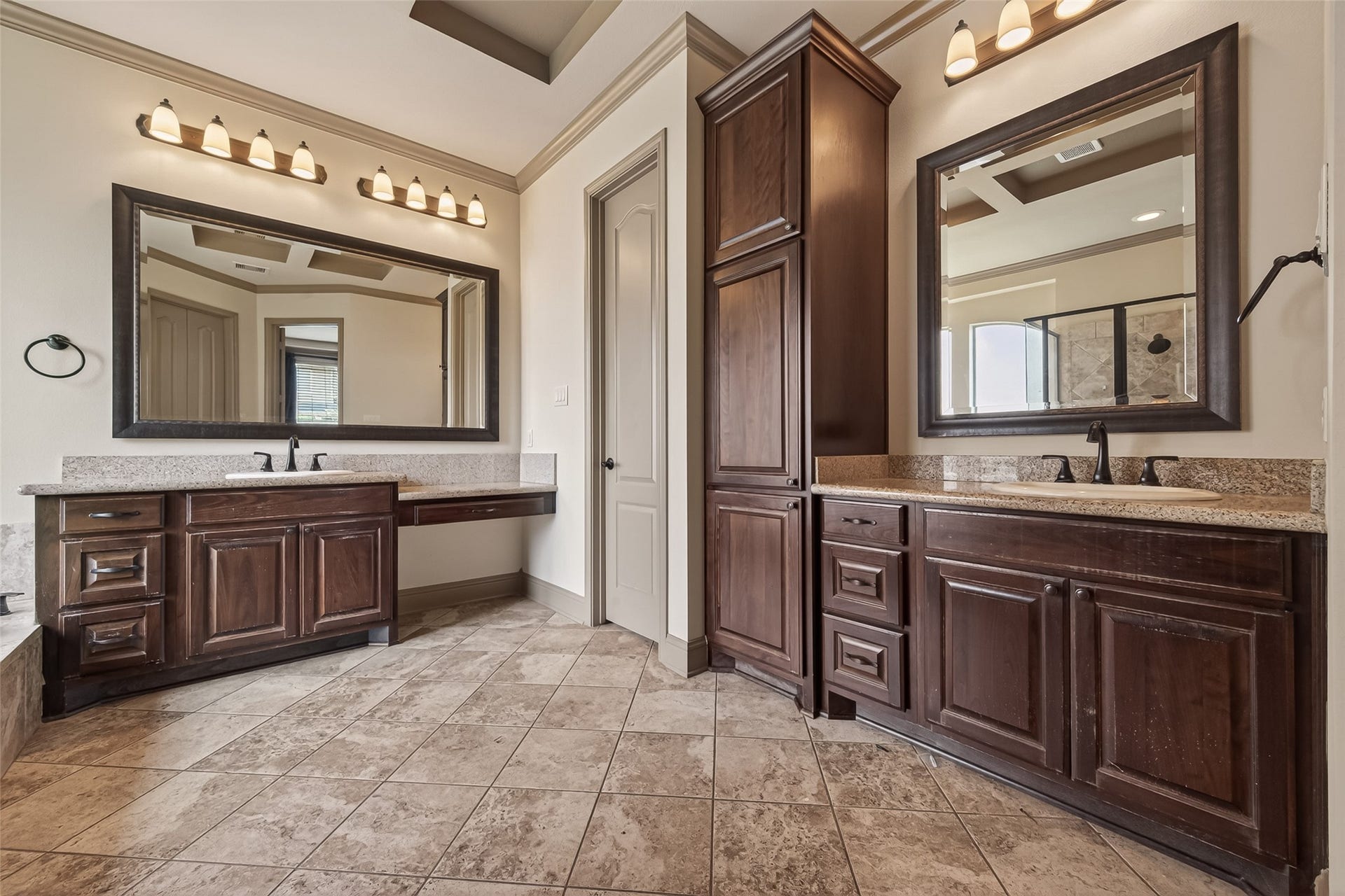 27411 Manor Falls Lane, Fulshear, TX 77441 Dual vanities with granite countertops and framed mirrors provide ample space for morning routines. A floor to ceiling wood linen tower between the vanities adds abundant storage. Oil rubbed bronze fixtures and warm vanity lighting complement the rich cabinetry, creating a sophisticated and well appointed retreat.