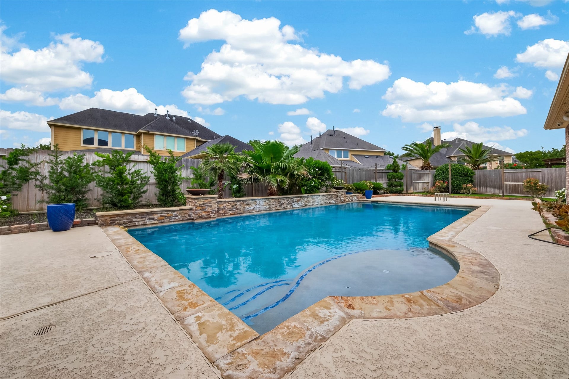 27411 Manor Falls Lane, Fulshear, TX 77441 Step into your own backyard oasis, where a sparkling pool with a beautiful stone coping surround invites warm-weather enjoyment. Lush tropical landscaping, including mature palm trees and evergreen shrubs, frames the fully fenced yard, creating a private and resort-like atmosphere. The generous pool deck provides ample space for lounge chairs and outdoor entertaining under the open Texas sky.
