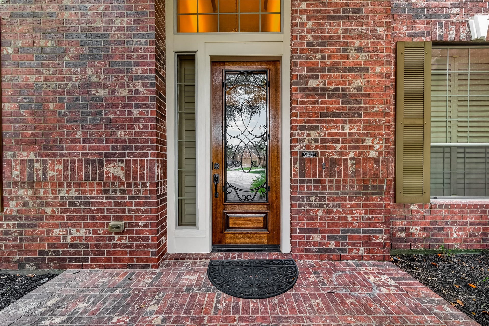 27411 Manor Falls Lane, Fulshear, TX 77441 A stunning solid wood front door with intricate wrought iron scrollwork and a glass panel makes a grand first impression. Flanked by a sidelite and topped with a transom window that glows with warm light, this entryway perfectly balances elegance and charm. The classic brick porch floor adds a timeless finishing touch, welcoming you and your guests in style.