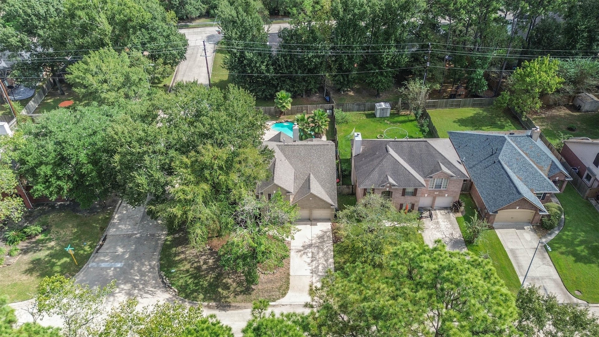 Enjoy a neighborhood landscape filled with mature trees, with your own pool waiting at home. This aerial perspective highlights the corner setting and the blend of leafy surroundings and backyard recreation.