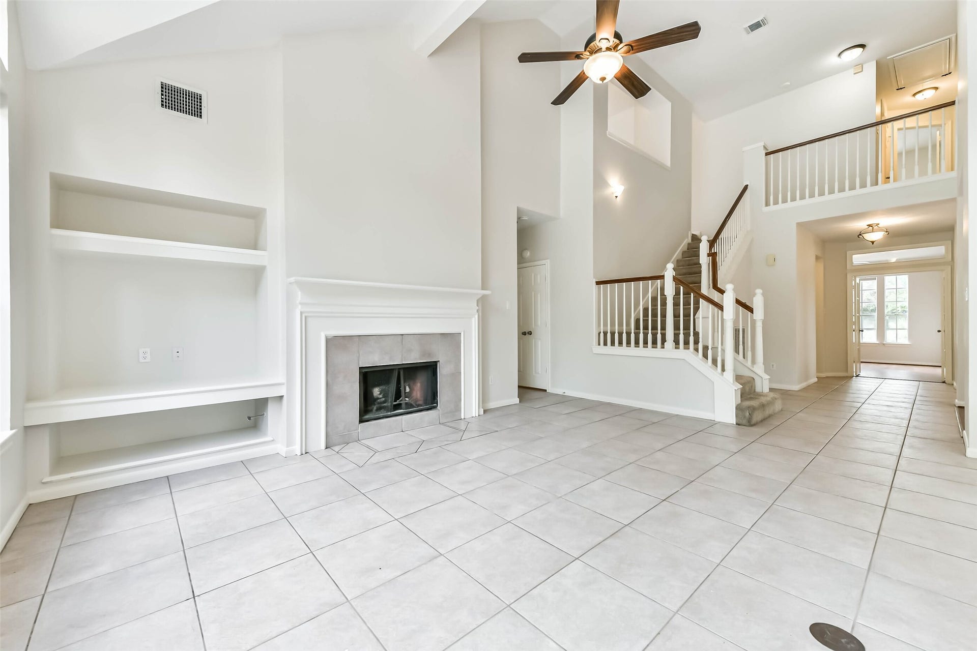 Picture your favorite seating gathered around the fireplace, with built-in shelving ready for books and personal treasures. The vaulted ceiling and open staircase give the room a spacious feel, while neutral finishes let your style take the lead.