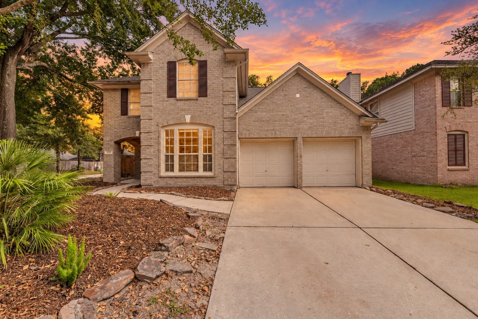 Come home to classic brick charm beneath a Texas sunset. Mature trees frame the two-story exterior, while the covered entry offers a welcoming arrivala beautiful setting for the next chapter of life at home. Sky digitally enhanced.