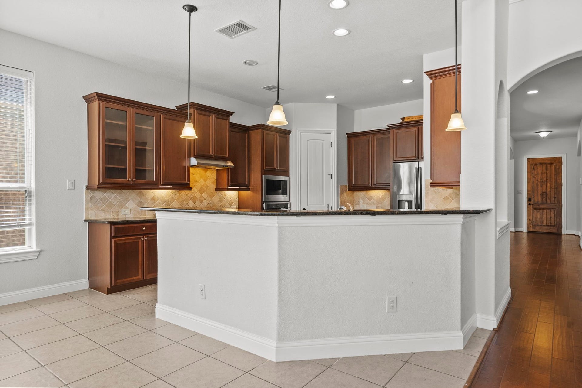 26111 Tintagel Lane, Kingwood, TX 77339 Spacious kitchen bar seating overlooks a beautifully appointed workspace with rich cabinetry, stylish pendant lighting, and easy flow into the home's hardwood-lined hallway!