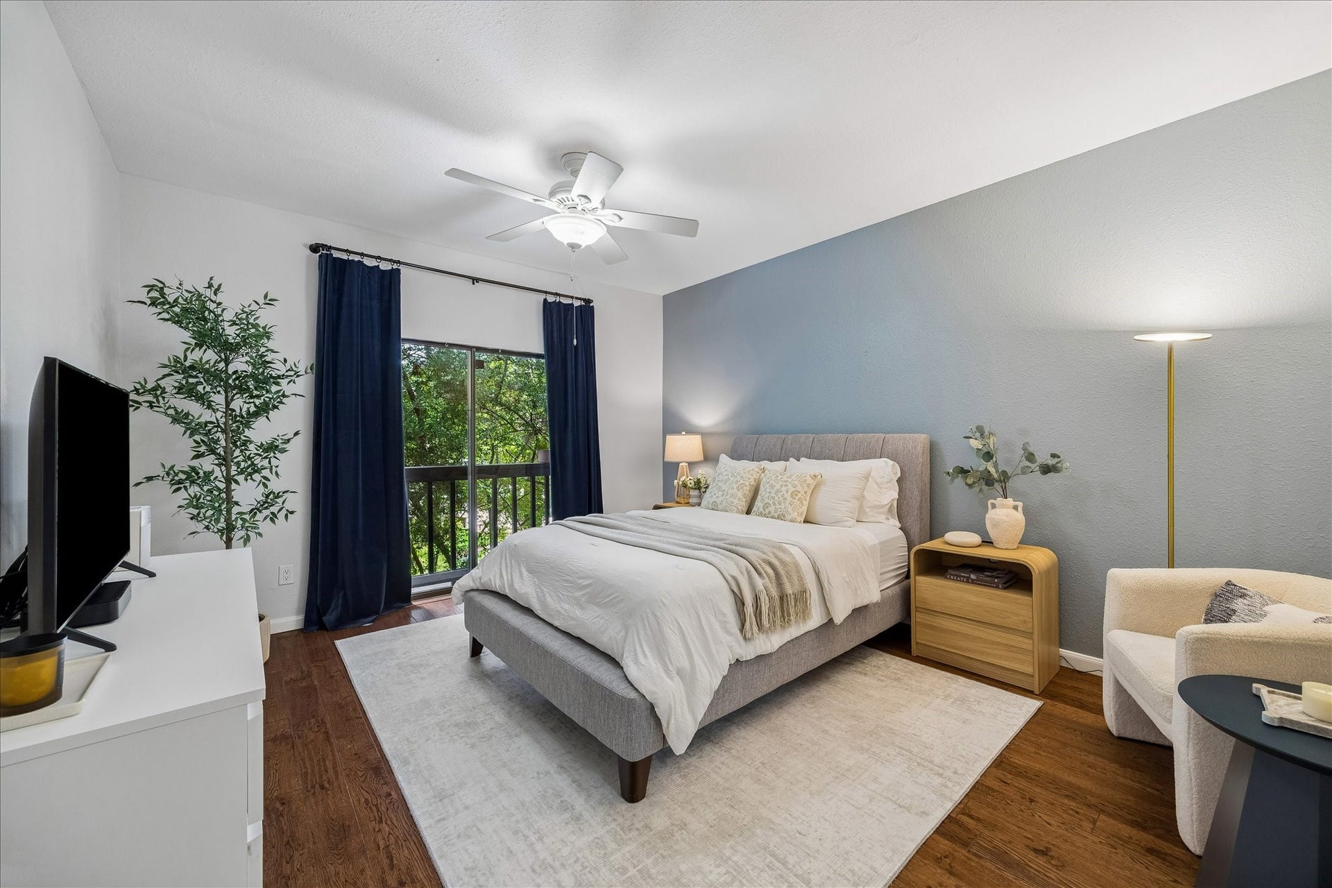 Spacious primary bedroom with sliding glass doors opening to a small balcony and peaceful tree-lined views.