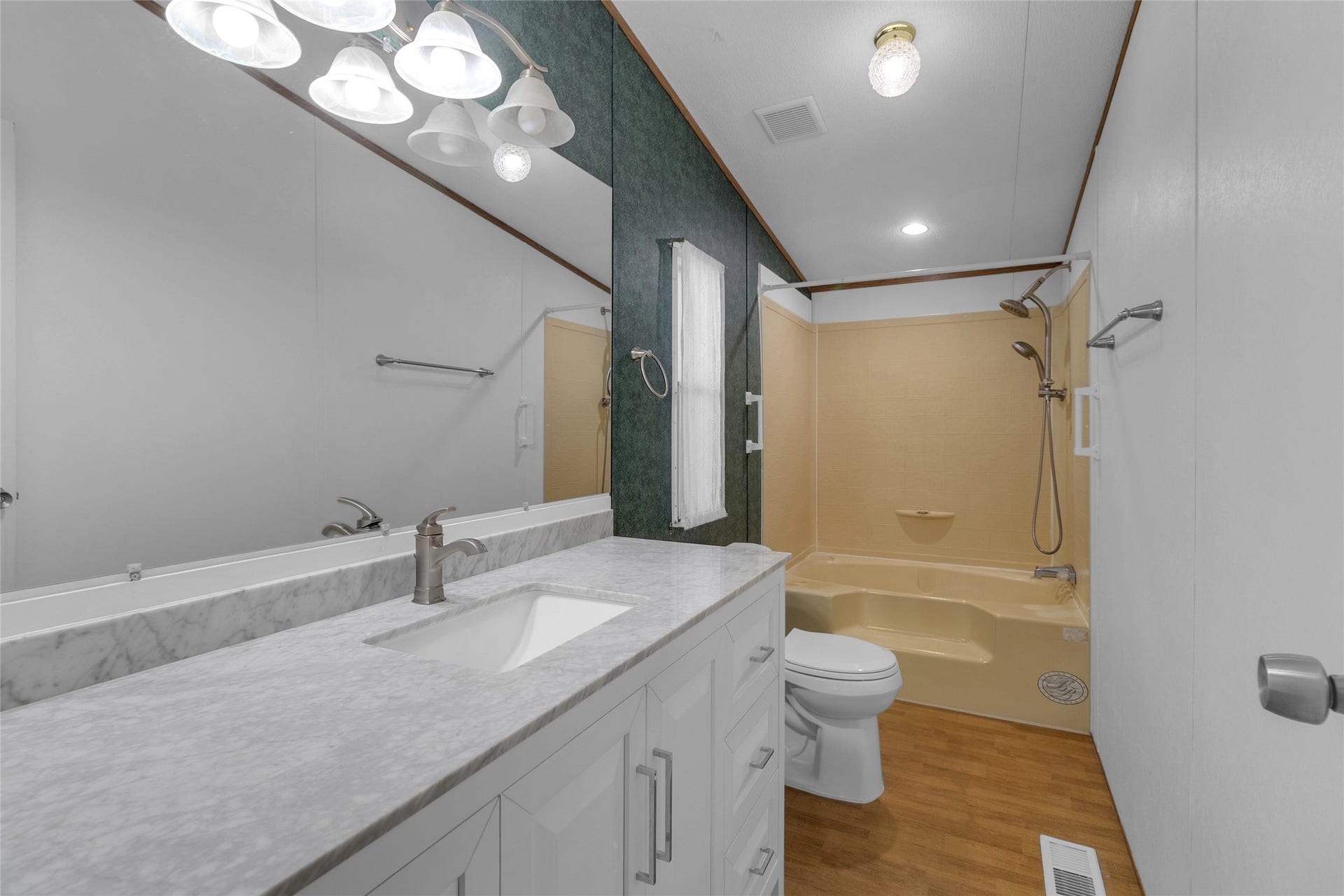 This bathroom features a clean, modern design with a white vanity and granite countertop, complemented by a large mirror and overhead lighting. It includes a bathtub with a shower.