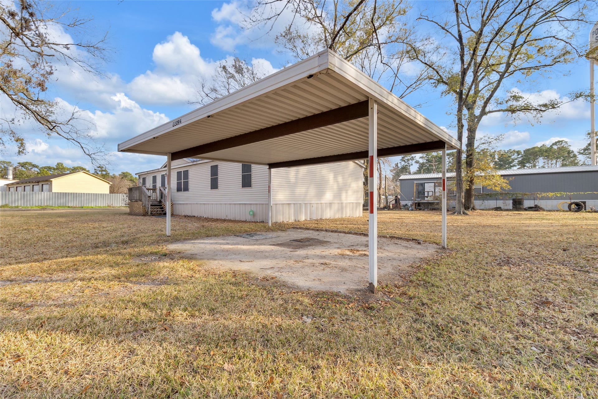 Metal carport in a spacious yard. The area is open and grassy, ideal for outdoor activities.