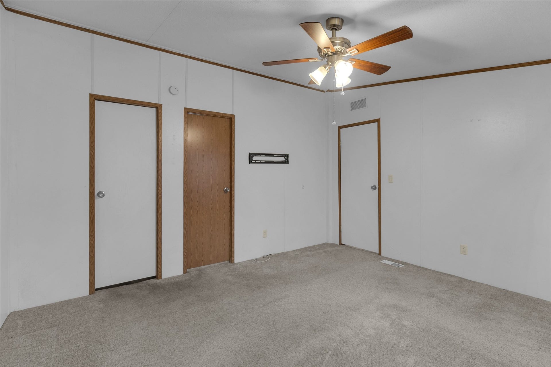 This room features neutral carpet and walls, a ceiling fan with lights, and three wooden doors, offering a versatile space for customization.
