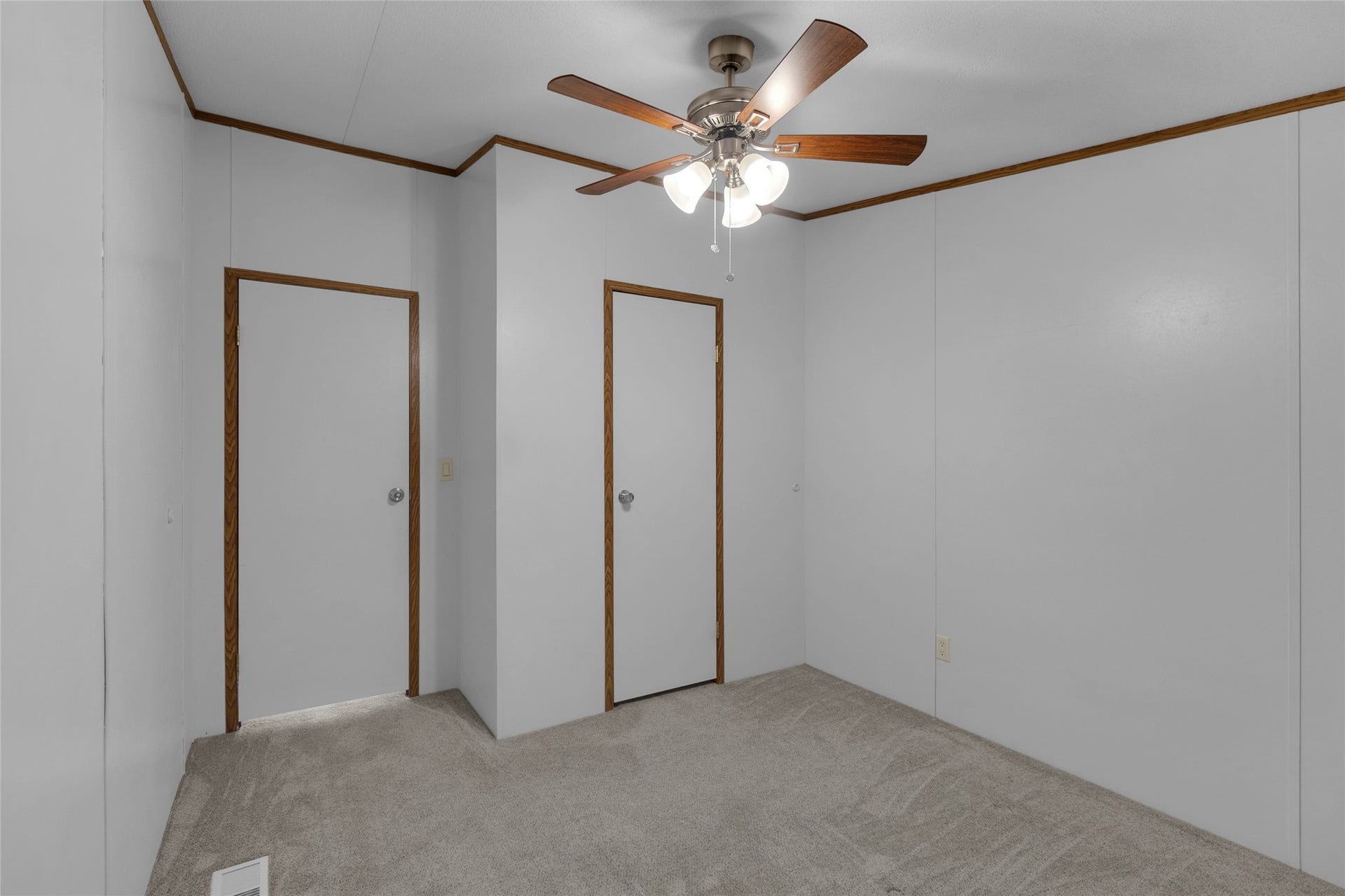 The third bedroom showcases neutral colored walls complemented by wood trim and carpeted flooring. It features a ceiling fan with lighting and two doors, one providing access to the room and the other leading to a conveniently sized, functional closet.