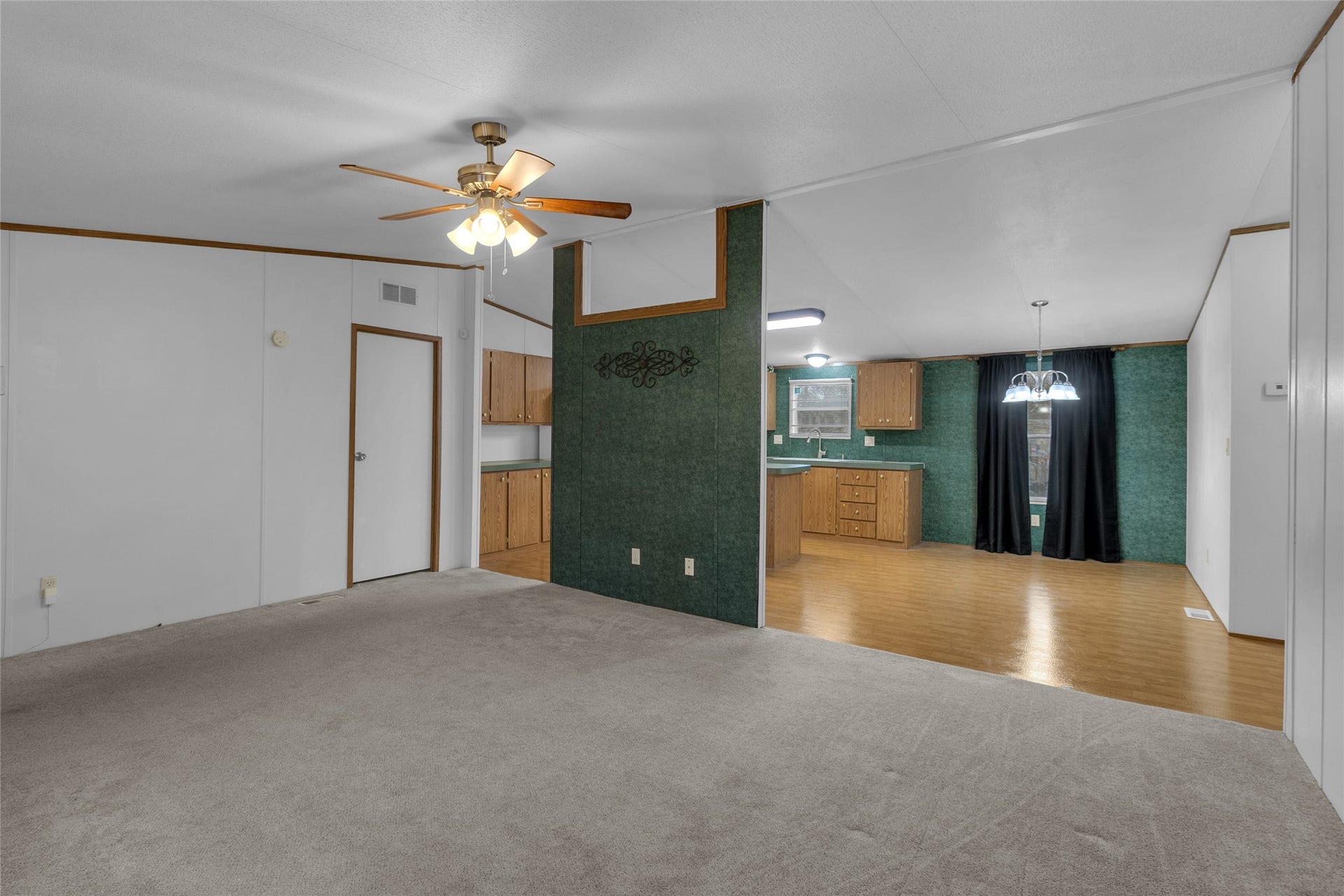 This spacious living area  opening into the kitchen with wood cabinetry and laminate flooring. The dining area is accented by an overhead light fixture.