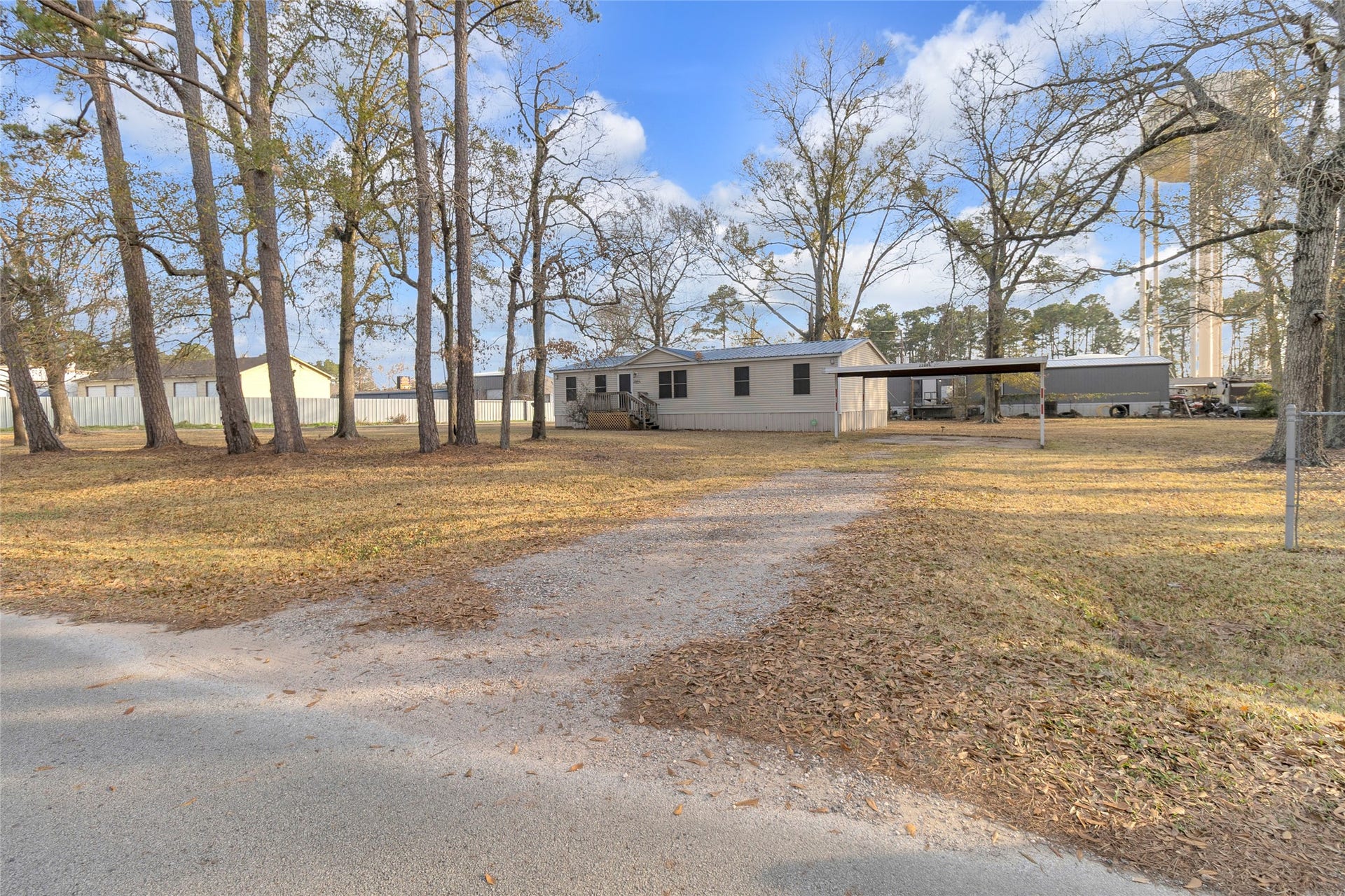 Tree-filled yard and a gravel driveway leading up to a carport. The setting is open and peaceful, with a mix of trees and open lawn areas.