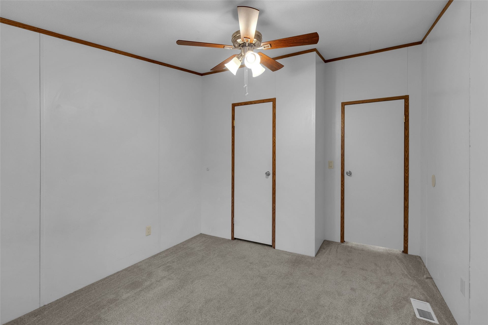 The second bedroom showcases neutral-colored walls complemented by wood trim and carpeted flooring. It features a ceiling fan with lighting and two doors, one providing access to the room and the other leading to a conveniently sized, functional closet.