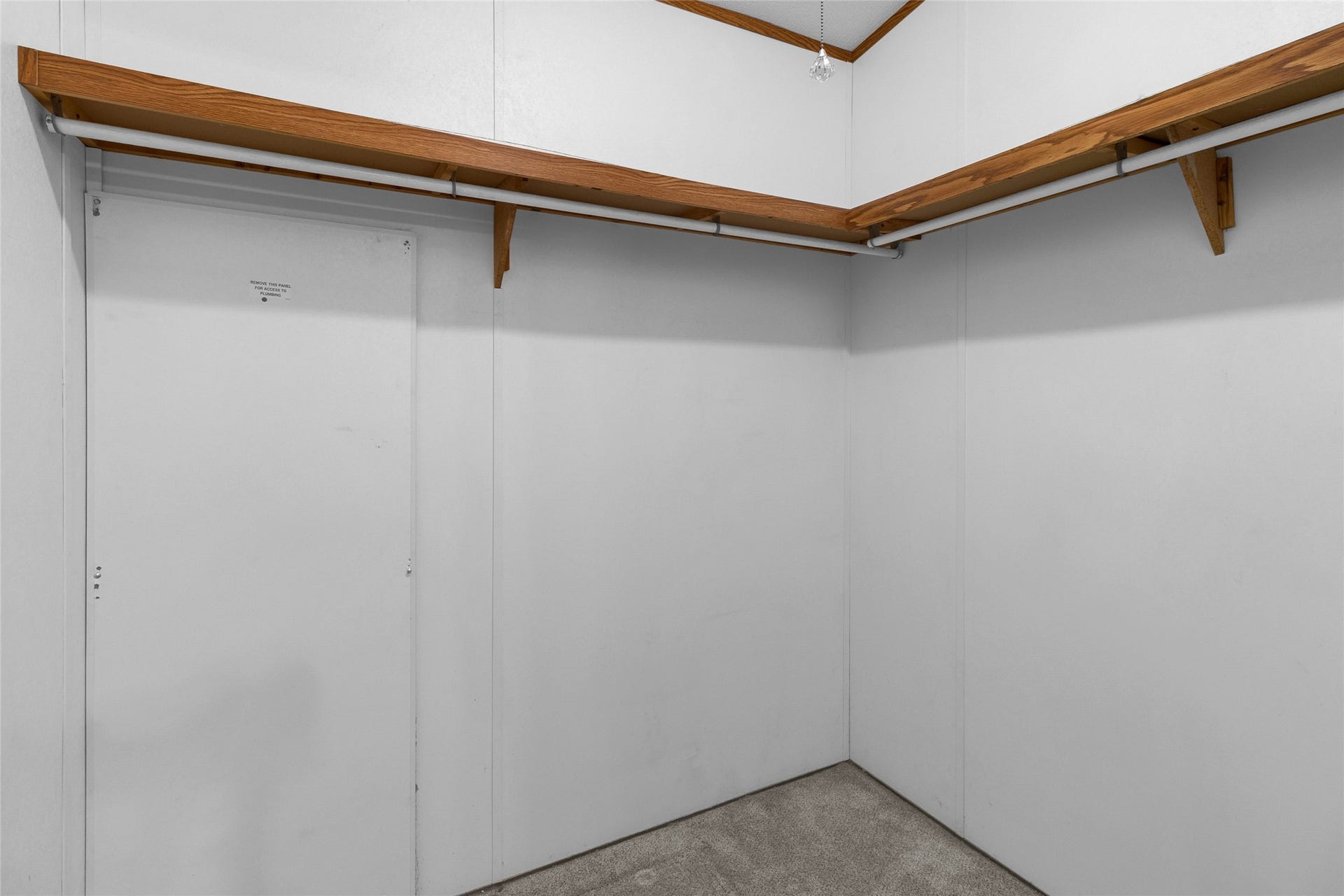 Primary spacious walk-in closet with white walls, featuring wooden shelves and hanging rods, perfect for organizing clothing and accessories.