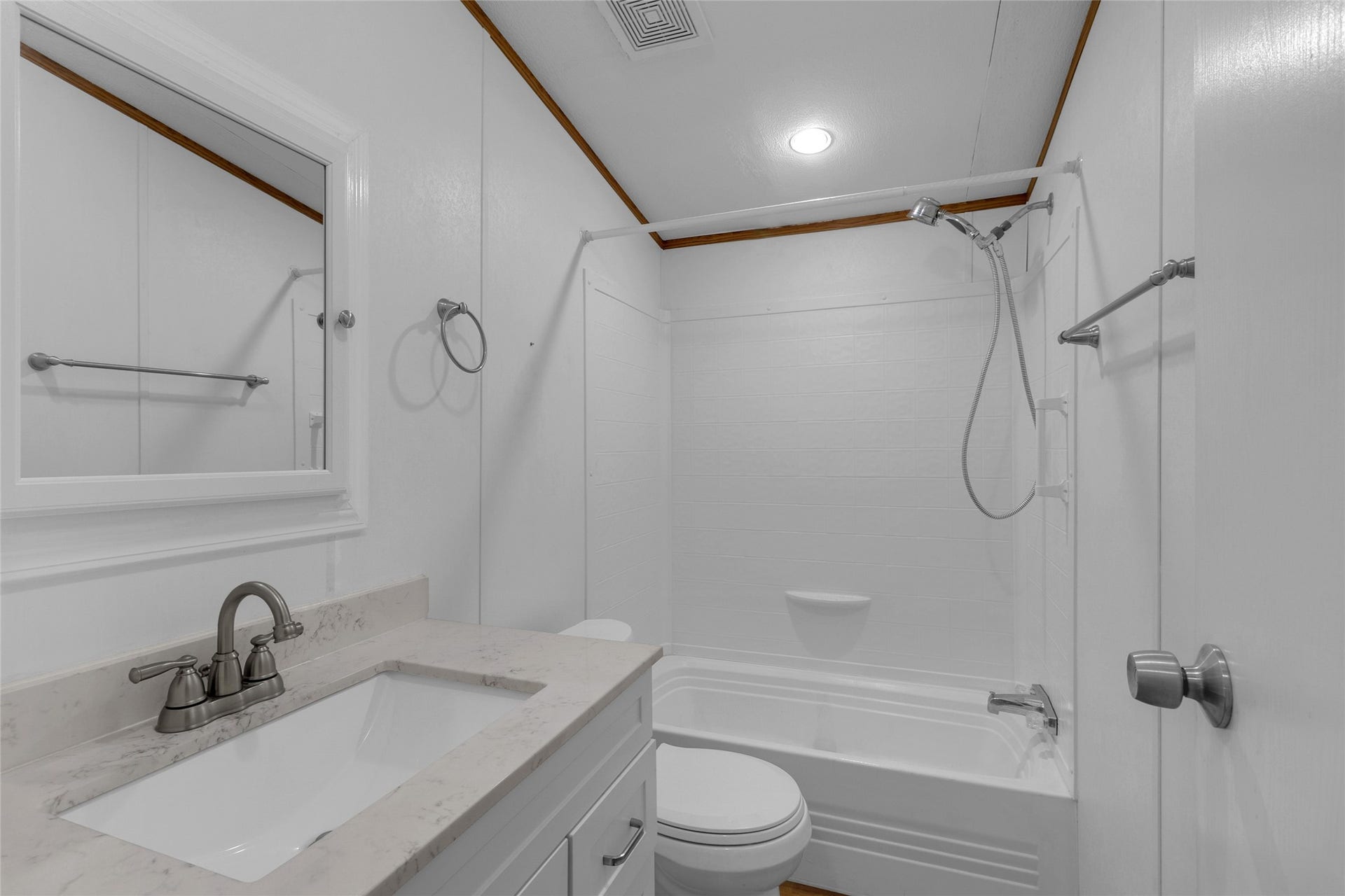 This bathroom features a clean, modern design with white walls and a contrasting wood-trim ceiling. It includes a sleek vanity with a marble countertop, a built-in mirror, and a combined shower and bathtub. Chrome fixtures add a touch of elegance.