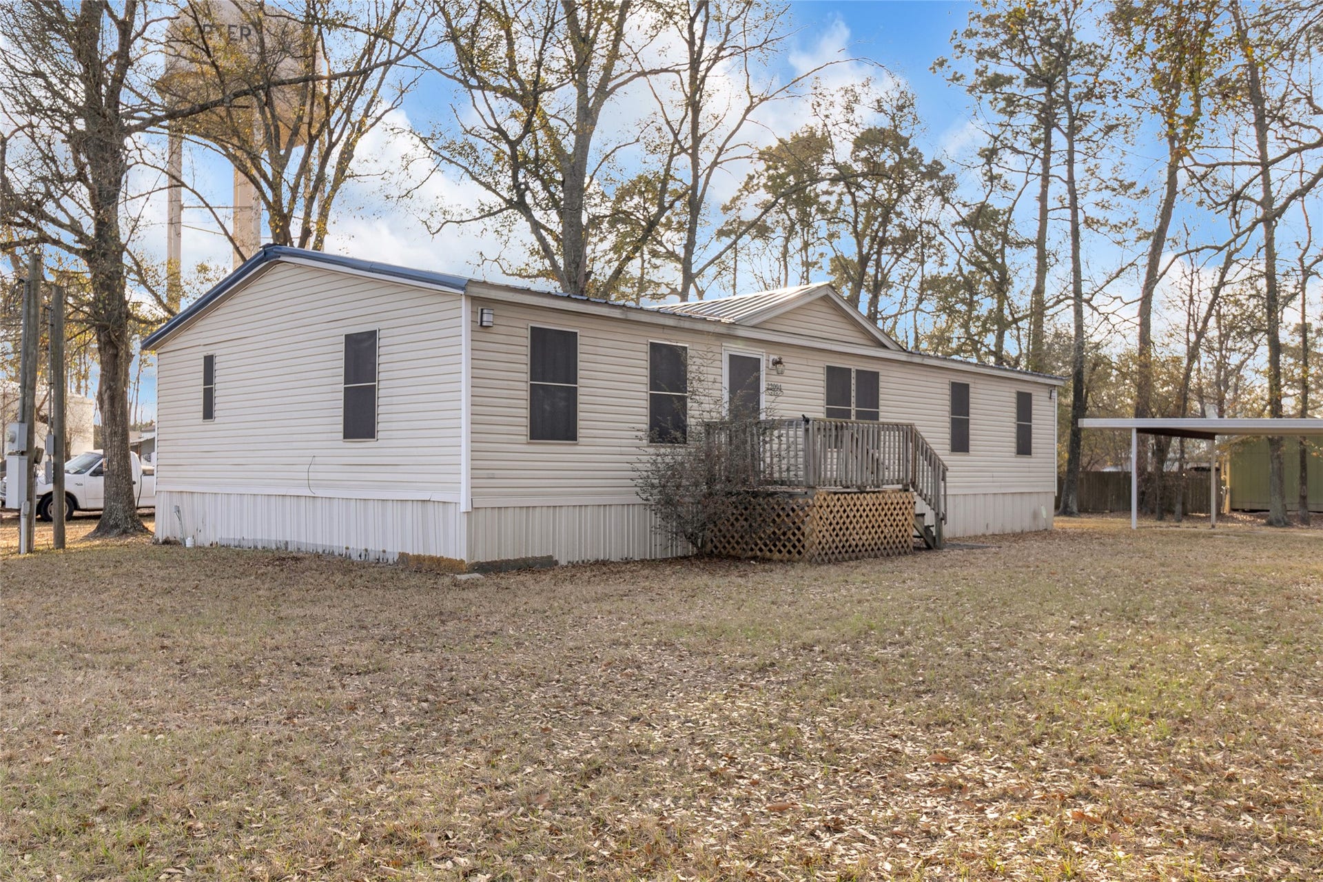 Small deck, situated on a spacious, grassy lot surrounded by trees, offering a peaceful setting.