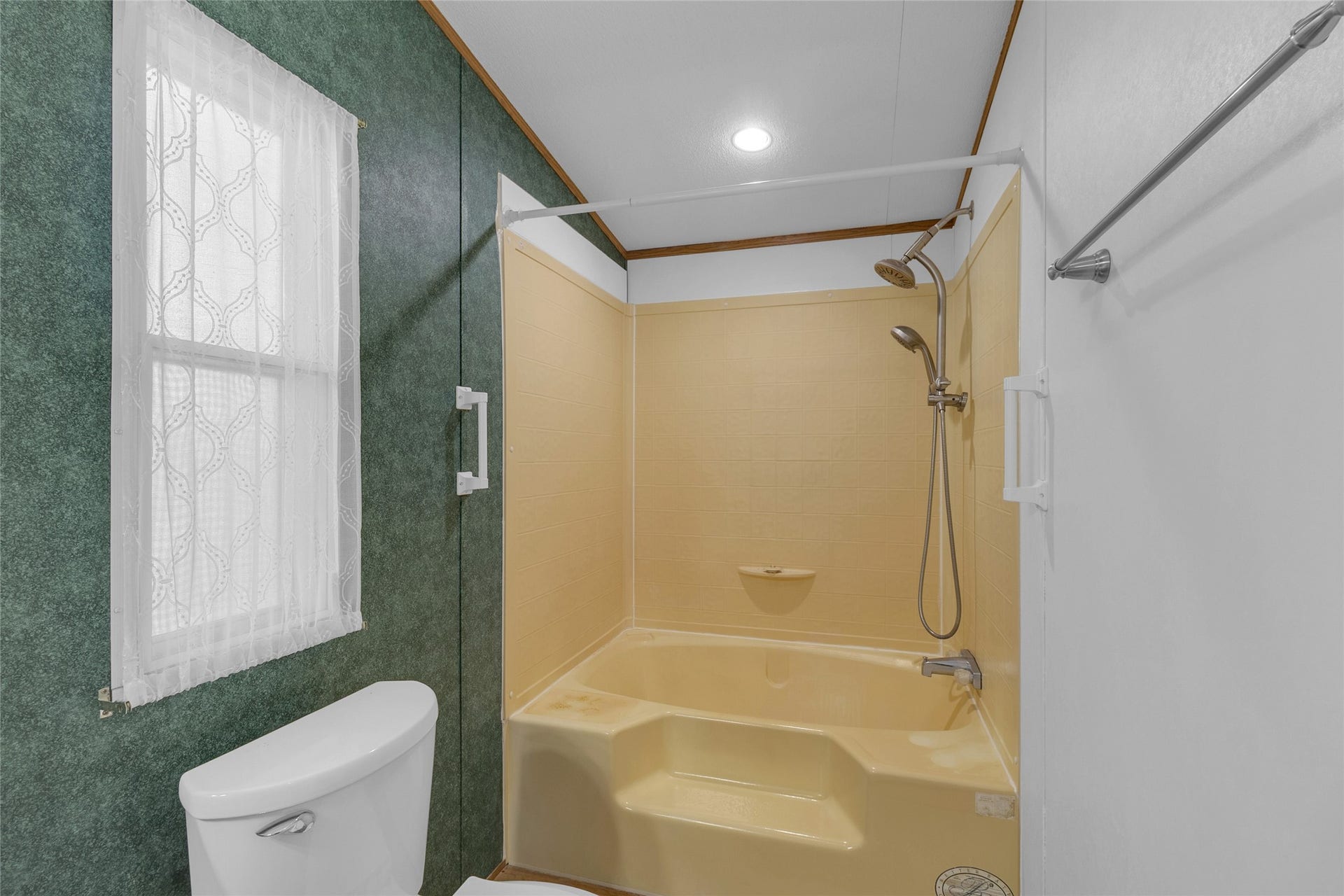 This bathroom features a bathtub with a shower, surrounded by green textured walls.