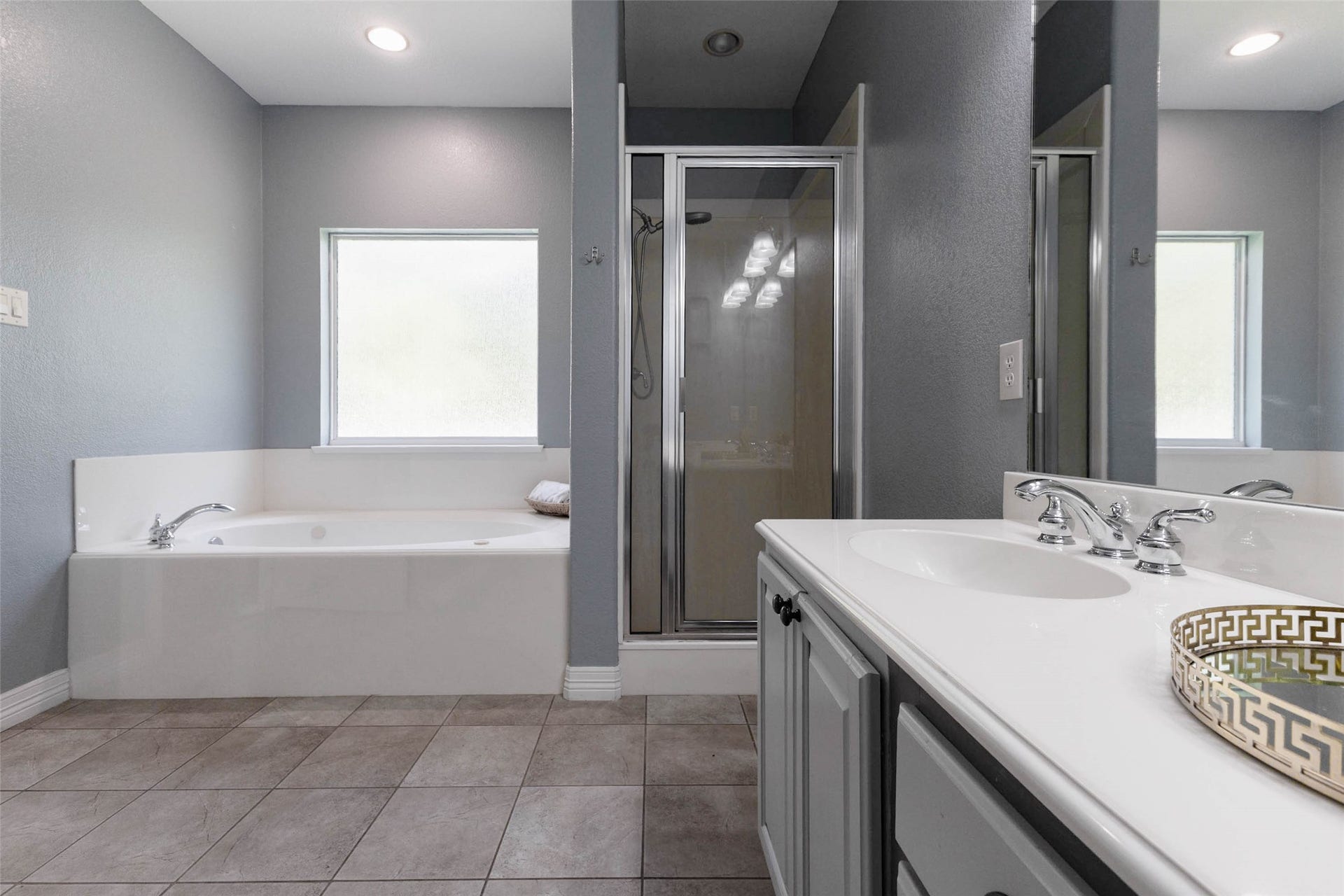 346 Skylark Street, Magnolia, TX 77355 The primary bath offers a jetted tub beneath a frosted glass window, a separate glass-enclosed shower, spacious vanity, and tile flooring.