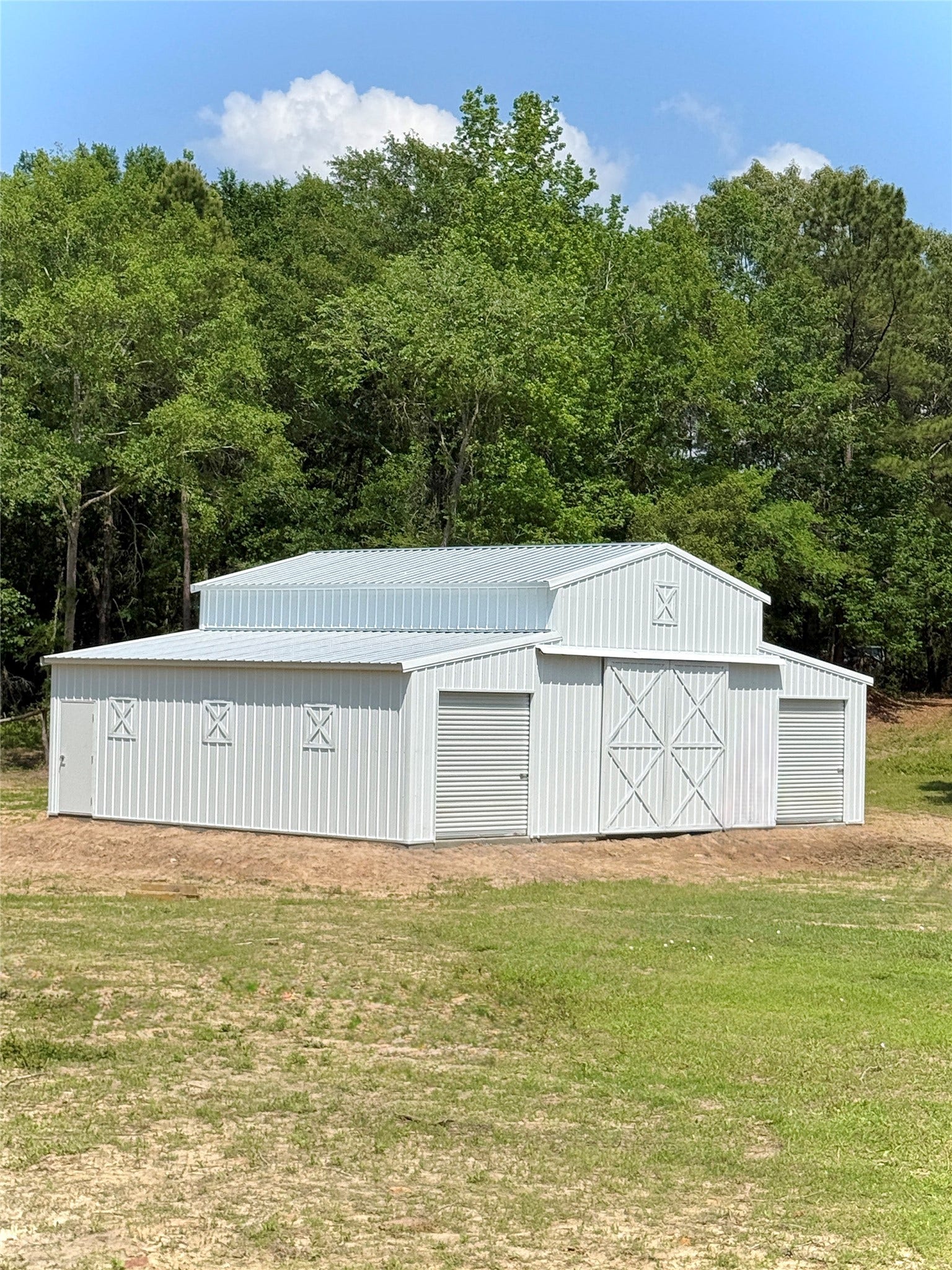 Spacious metal barn with rolling doors and classic design, set against lush greenery, perfect for storage or equestrian needs.