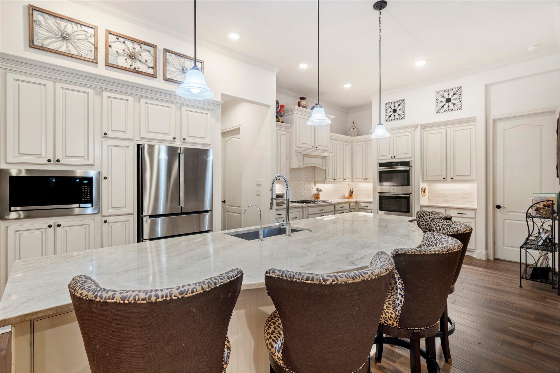 Elegant kitchen featuring a large marble island with seating, stainless steel appliances, and custom cabinetry, all under stylish pendant lighting.