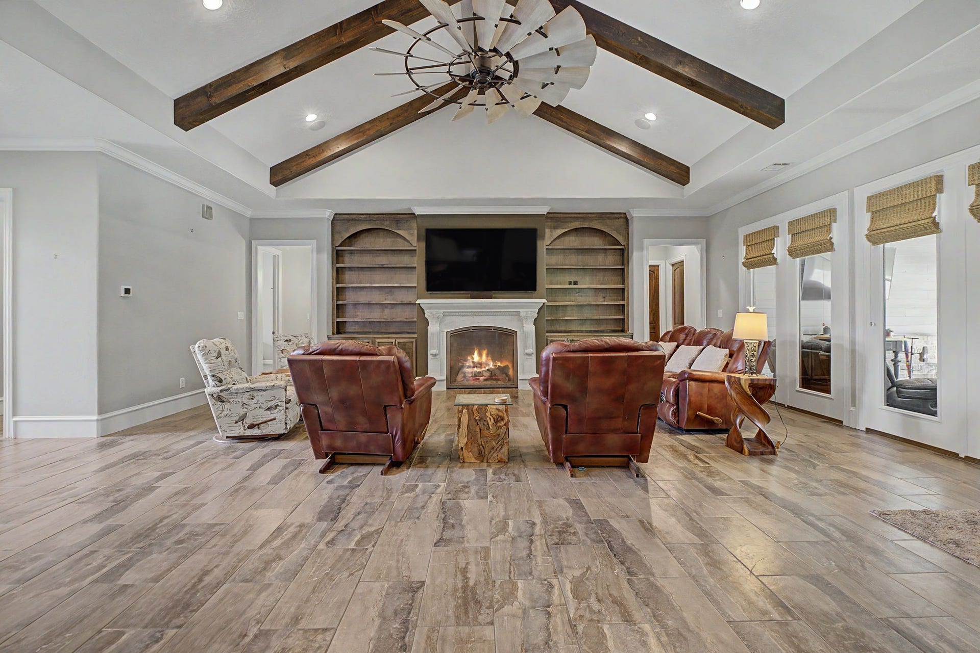 11865 Hope Lane, Magnolia, TX 77354 Alternate view of the living room showcasing the custom built-ins, stunning wood beams, and durable tile flooring. And don't miss the impressive statement ceiling fan overhead!