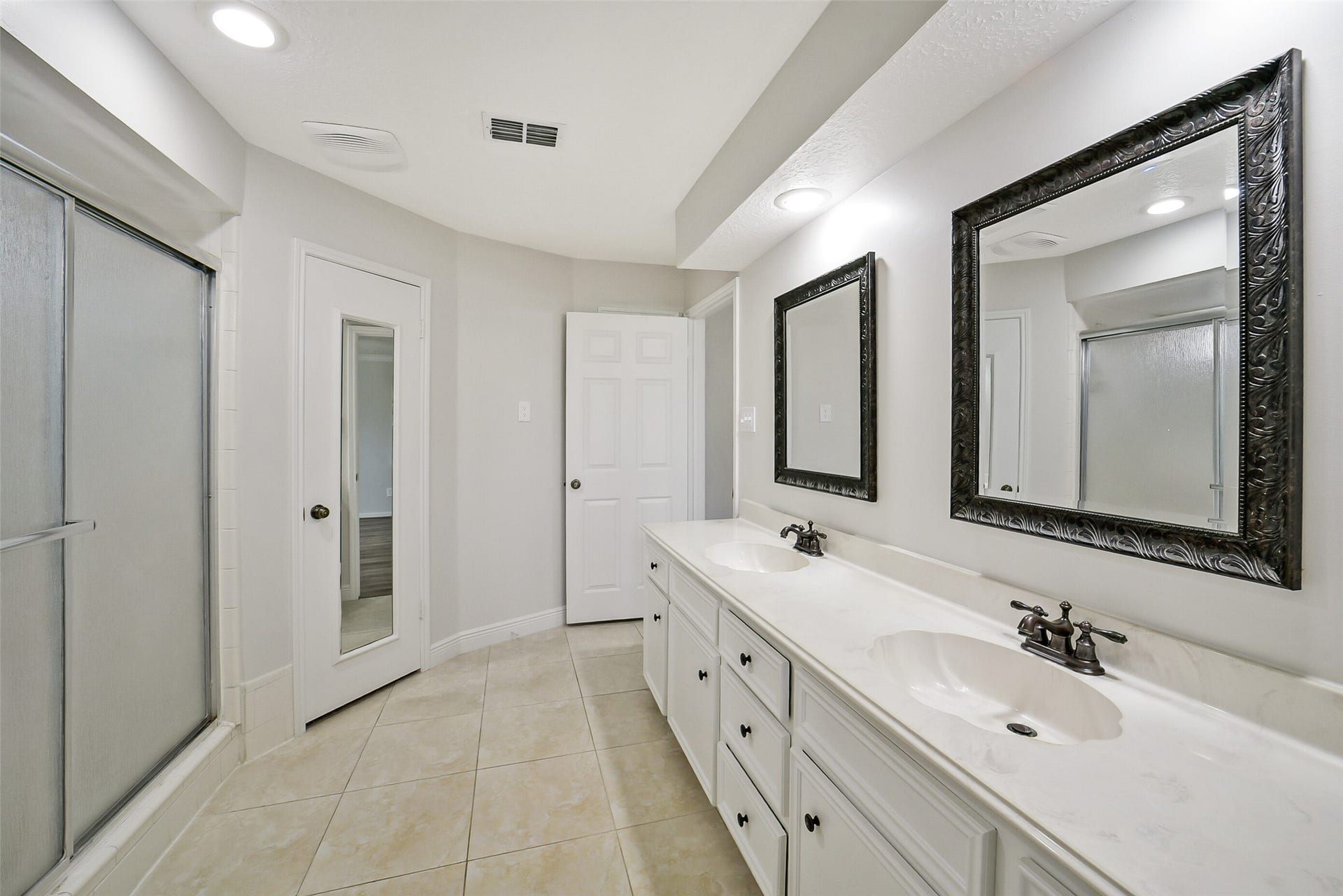 The primary bathroom showcases double sinks, two framed mirrors and tile floors.