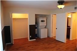 6001 Reims Road, #1202, Houston, TX 77036 This photo shows a room with hardwood flooring, a ceiling light, and a compact laundry area with a stacked washer and dryer. There are two open doorways leading to a closet and another room.