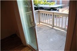 6001 Reims Road, #1202, Houston, TX 77036 This photo shows a small balcony accessible through a sliding glass door, offering outdoor space with a railing and a view of a tree and adjacent buildings.