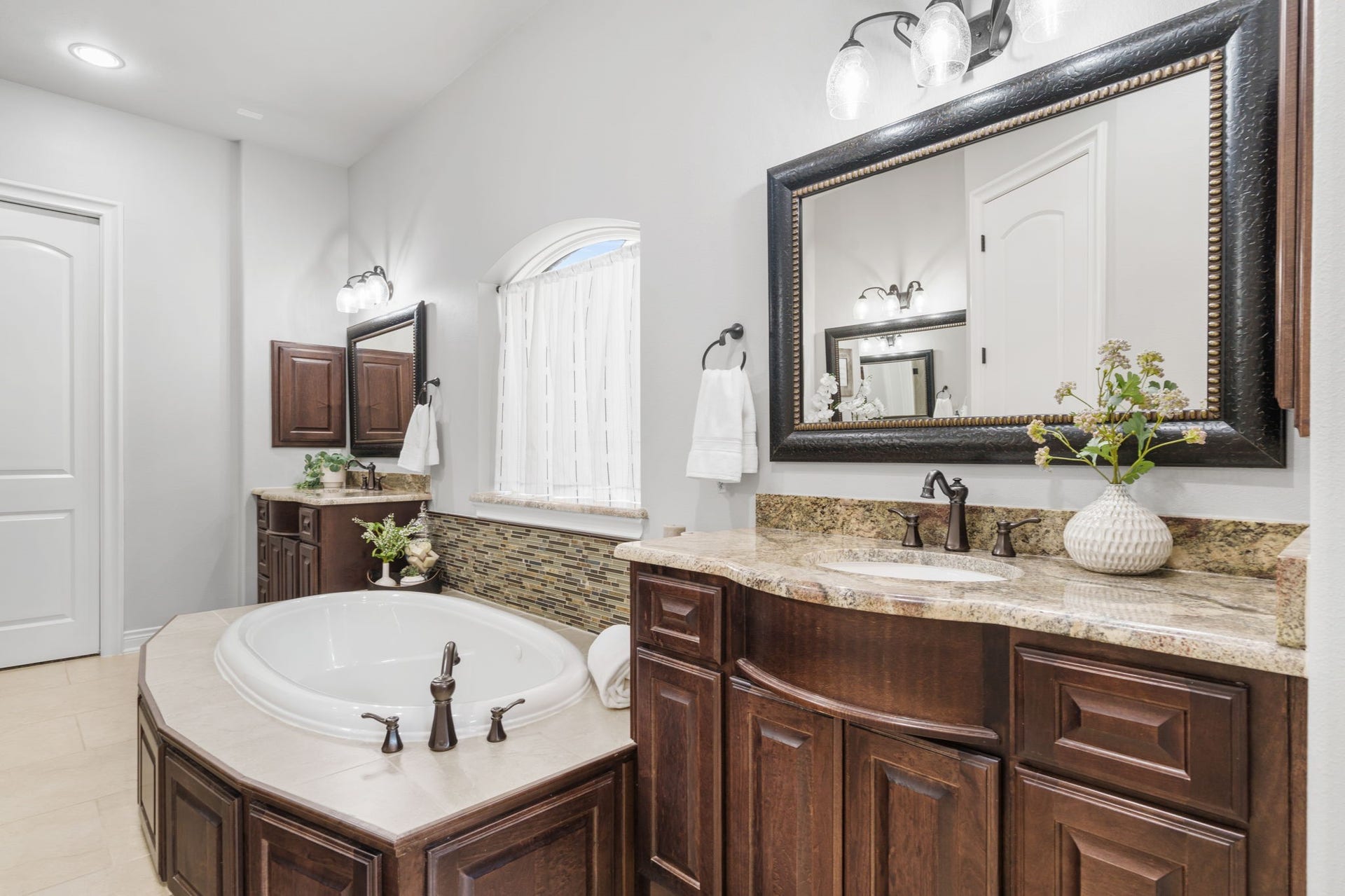126 Summer Holly Drive, Conroe, TX 77384 Spa-inspired primary bath featuring separate granite-topped vanities, rich cabinetry, and a spacious soaking tub.