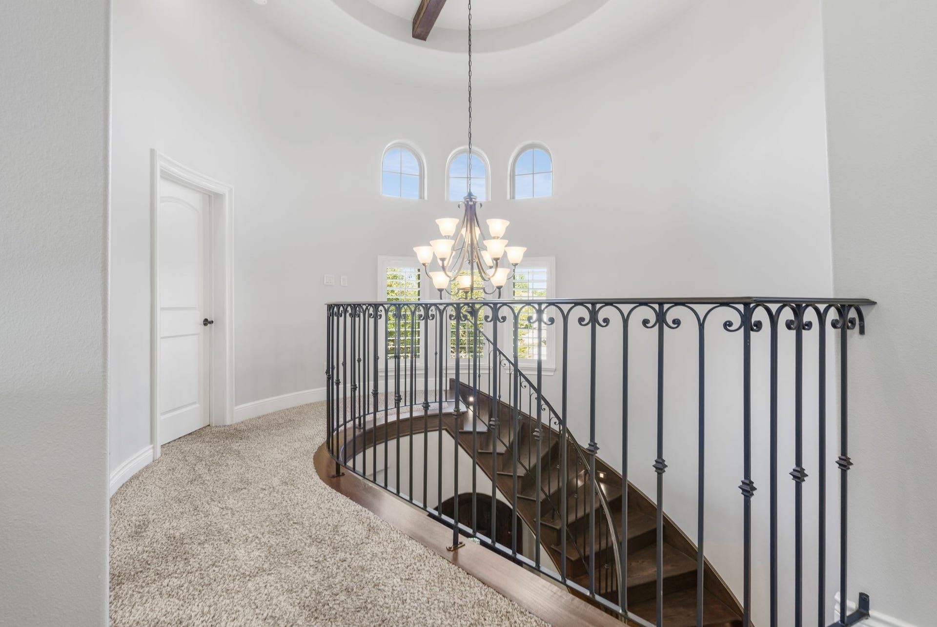 126 Summer Holly Drive, Conroe, TX 77384 Beautiful curved staircase opens to a bright second-floor landing featuring elegant wrought-iron railings, arched windows, and a statement chandelier.