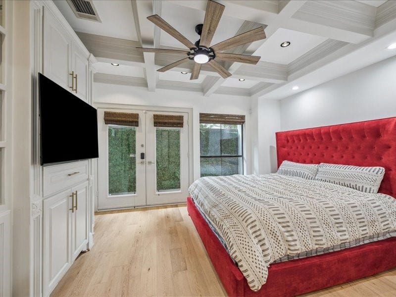 Unwind in a bedroom full of character, featuring detailed ceiling woodwork, built-in shelving, generous storage, and a ceiling fan for added comfort. A privacy fence and spacious backyard behind the room complete this inviting retreat.
