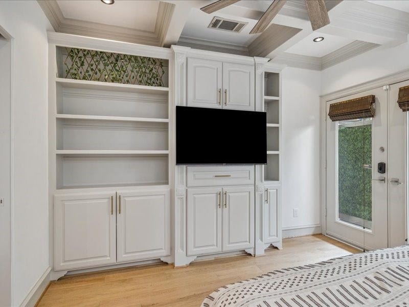 Unwind in a bedroom full of character, featuring detailed ceiling woodwork, built-in shelving, generous storage, and a ceiling fan for added comfort. A privacy fence and spacious backyard behind the room complete this inviting retreat.