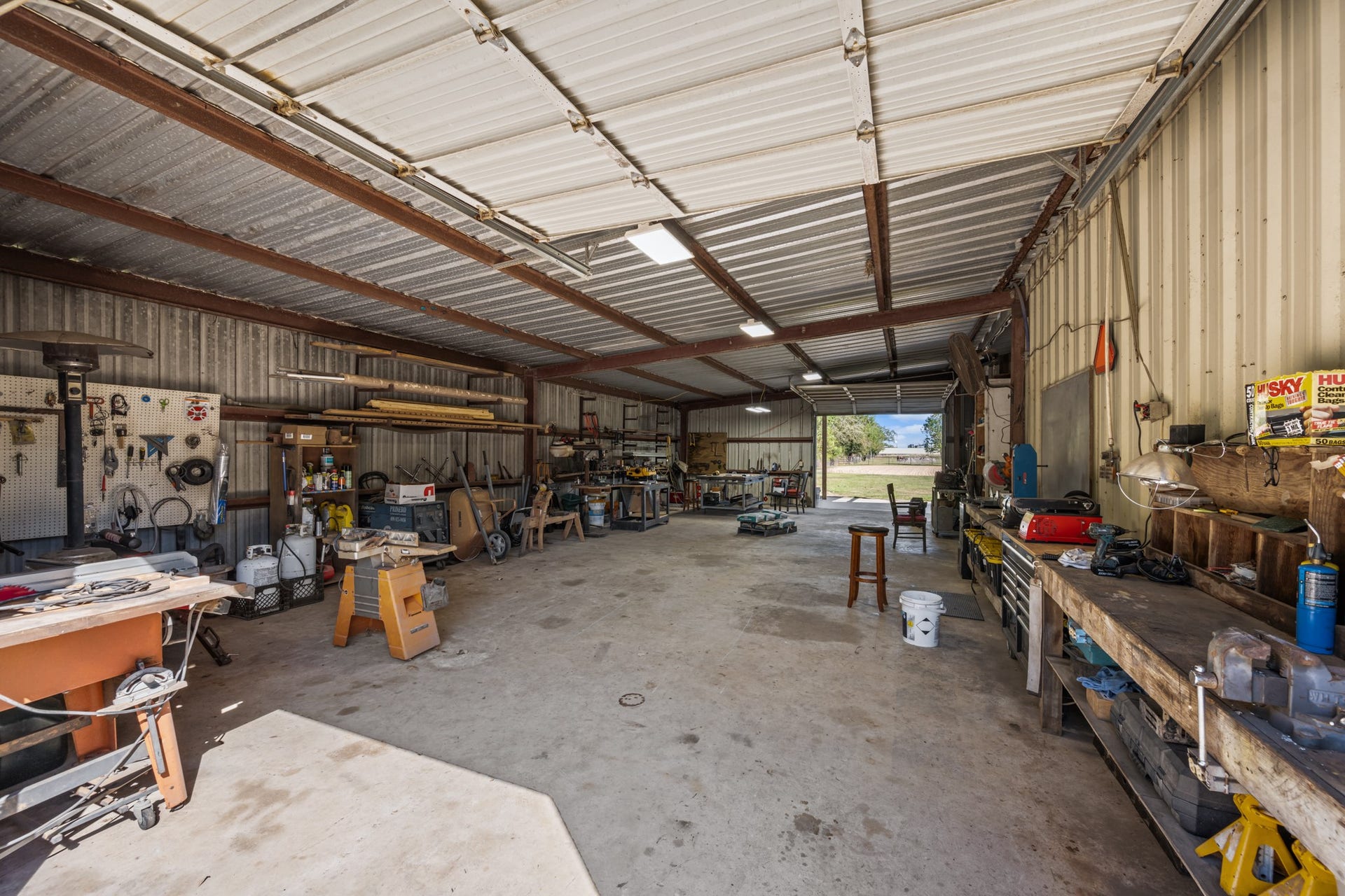 2215 Avenue Q, Santa Fe, TX 77510 Expansive metal workshop featuring concrete flooring, overhead lighting, exposed steel beams, multiple workbenches, and generous space for tools, equipment, and projects.