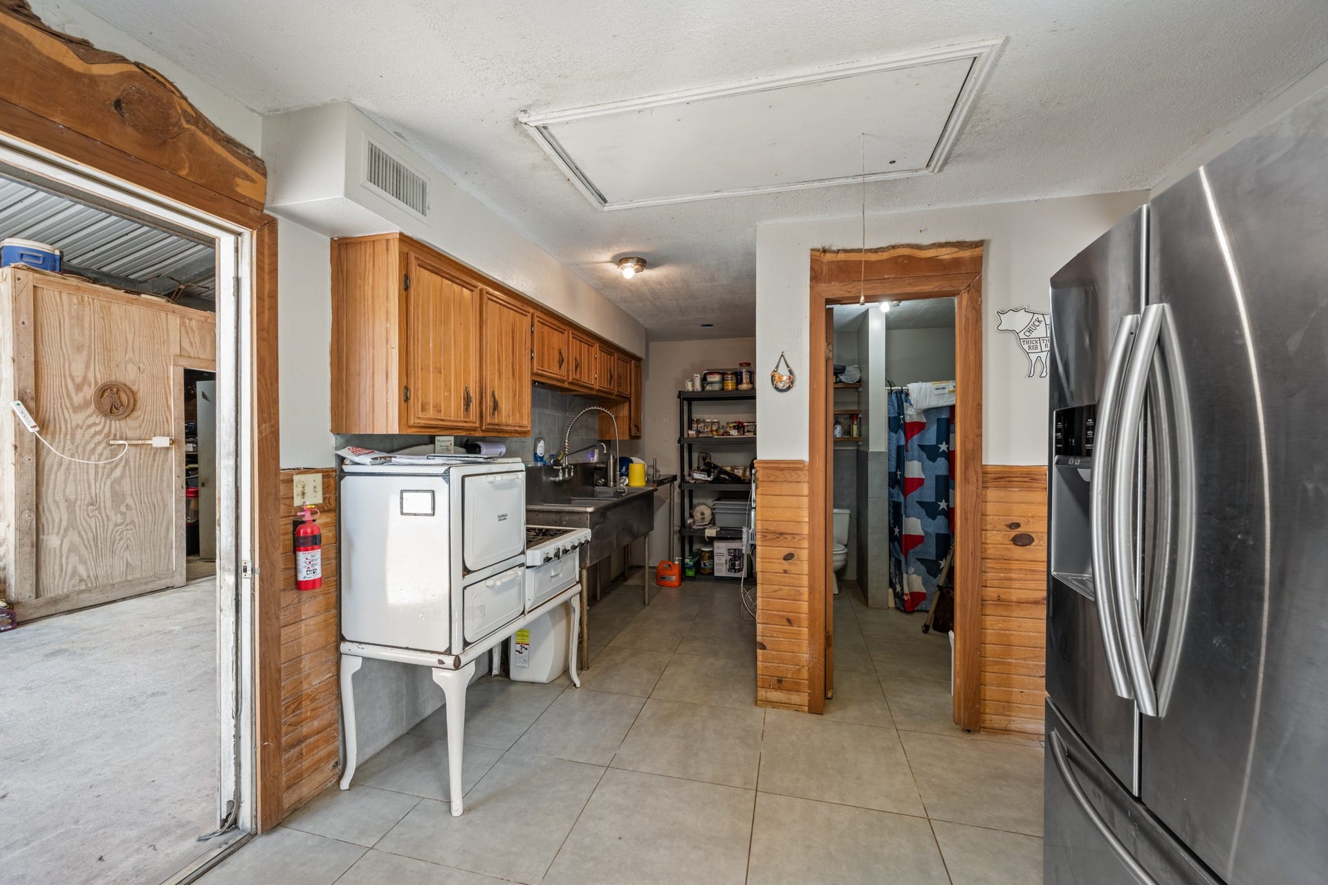 2215 Avenue Q, Santa Fe, TX 77510 Convenient secondary kitchen and utility space featuring wood cabinetry, stainless steel sink and work surfaces, tiled flooring, refrigeration, and an adjoining bathroom.