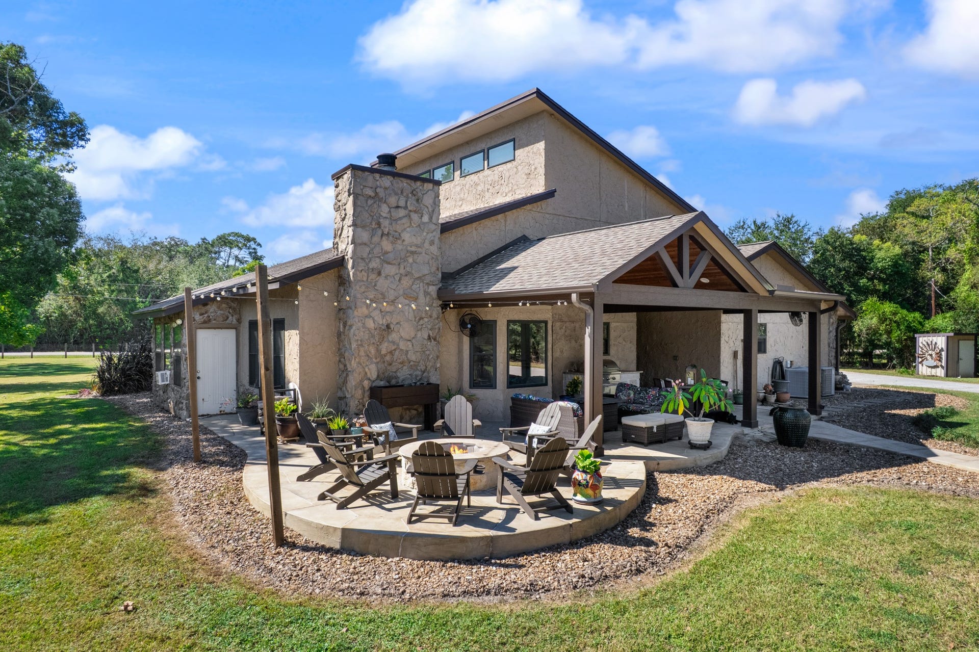 2215 Avenue Q, Santa Fe, TX 77510 Designed for entertaining, this expansive backyard retreat features a covered outdoor living and dining area, stone fireplace, and circular patio with a fire pit surrounded by Adirondack seating. Beautiful stone accents and mature trees complete this inviting outdoor setting.