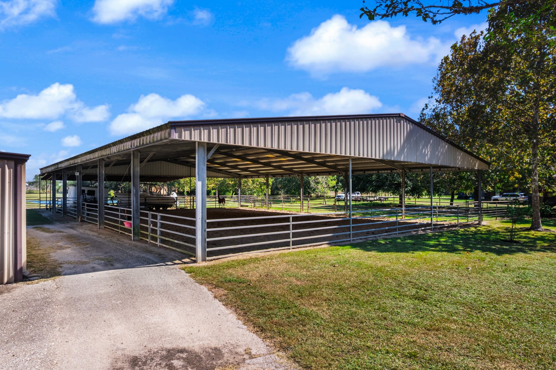 2215 Avenue Q, Santa Fe, TX 77510 Impressive covered equestrian arena featuring a soaring metal roof, open sides for natural ventilation, and sturdy metal panel fencing. The spacious riding and training area offers protection from the elements, providing a versatile setup for working horses, practicing riding skills, and enjoying equestrian activities throughout the year.