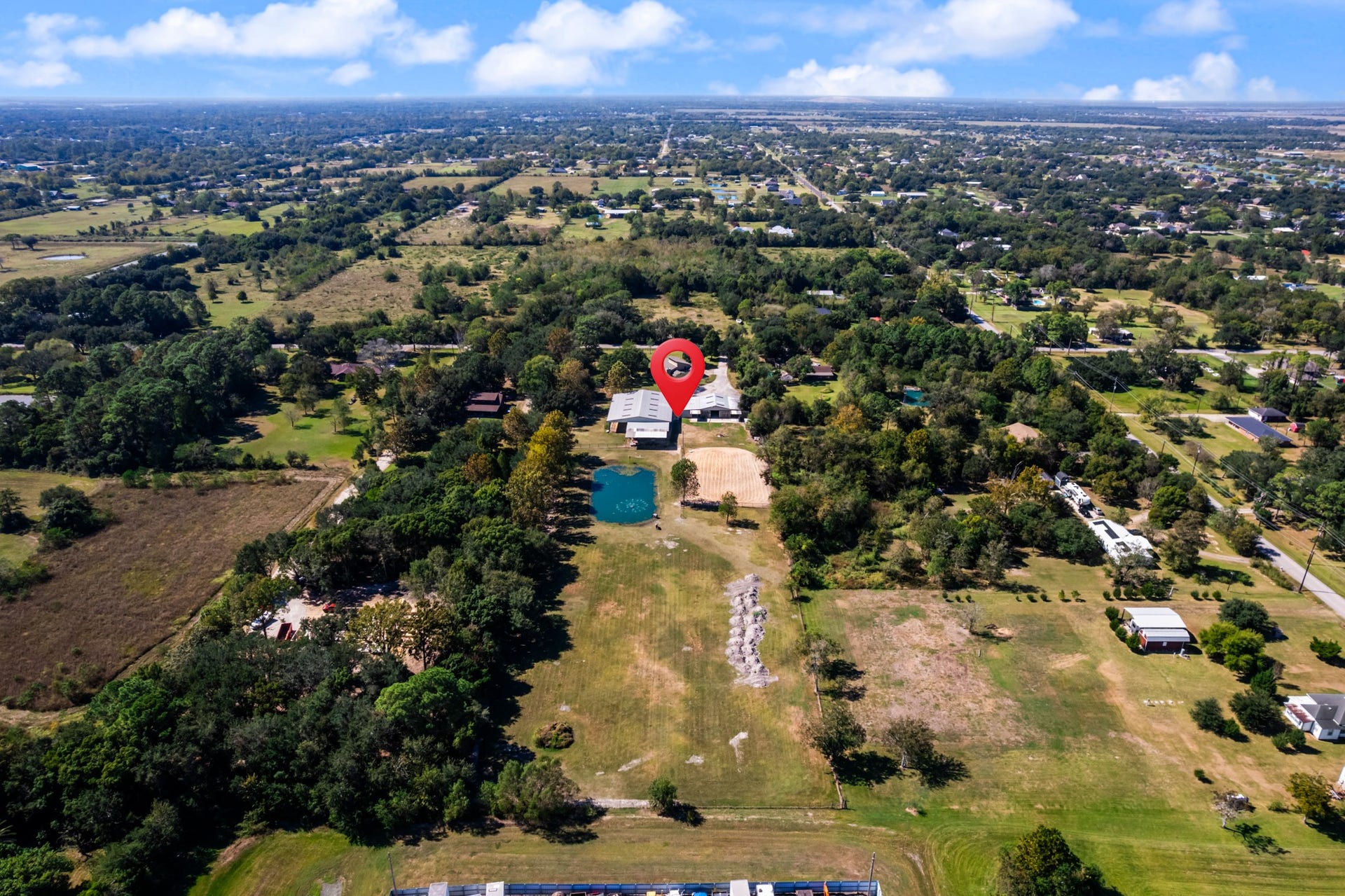 2215 Avenue Q, Santa Fe, TX 77510 A birds-eye view showcases the property's expansive grounds, featuring open pastureland, a picturesque pond, mature trees, and equestrian facilities. A beautiful blend of open space and natural surroundings offers plenty of room for horses, outdoor recreation, and enjoying the peaceful country setting while remaining close to nearby conveniences.