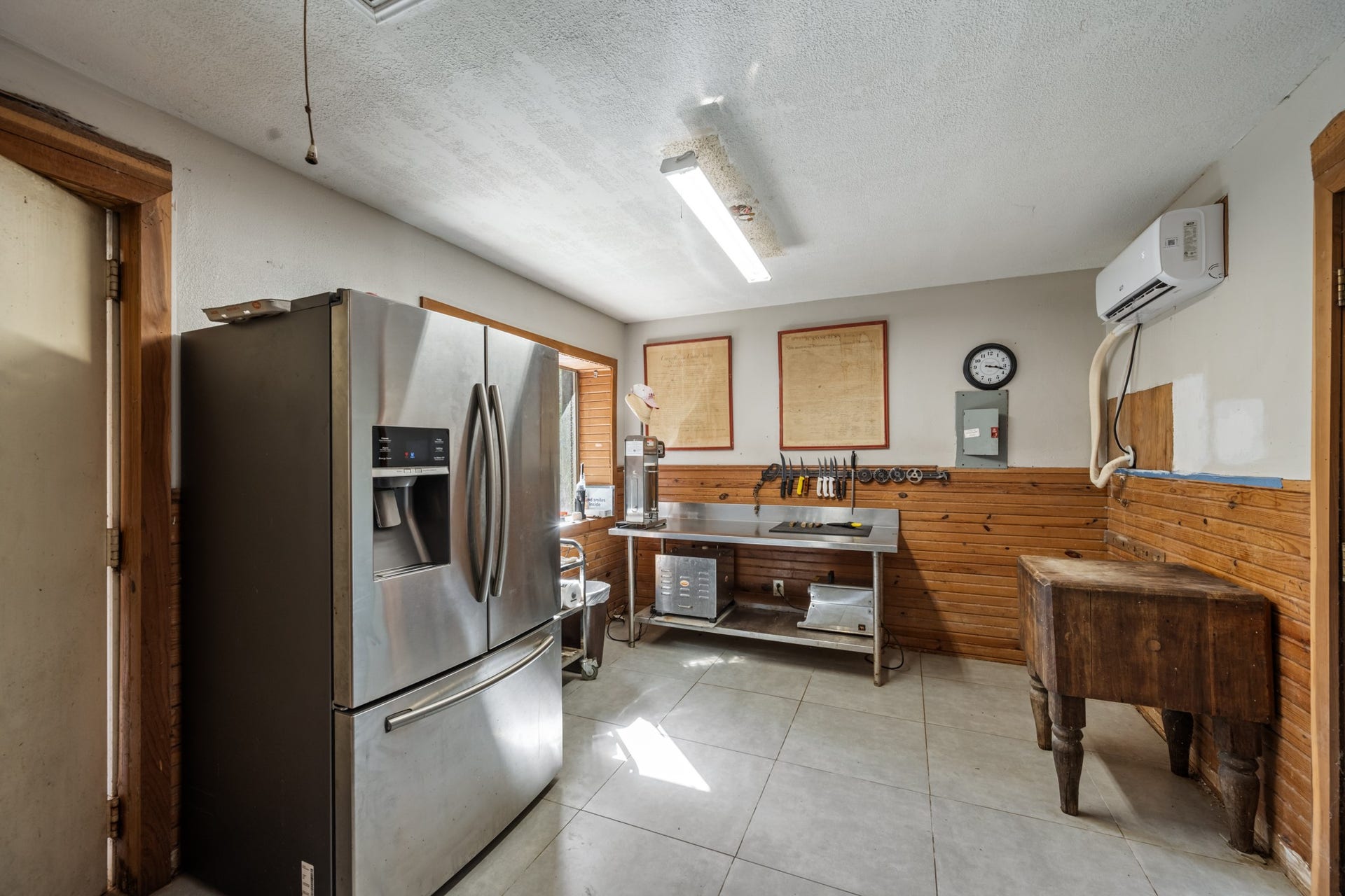 2215 Avenue Q, Santa Fe, TX 77510 Dedicated food preparation and utility space with stainless steel workstations, full-size refrigerator, butcher block table, tiled flooring, and wall-mounted mini-split system.
