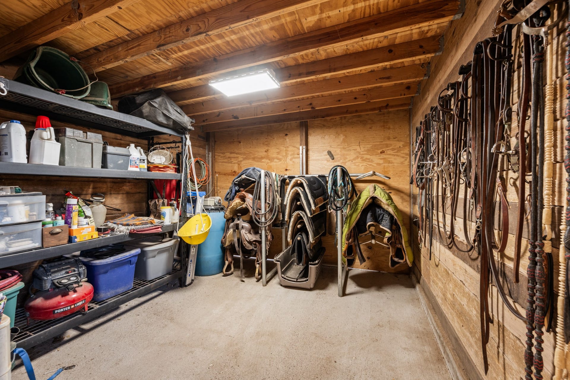 2215 Avenue Q, Santa Fe, TX 77510 Organized tack room featuring multiple saddle racks, wall-mounted bridle and rein storage, built-in shelving, and space for riding equipment and horse care supplies.