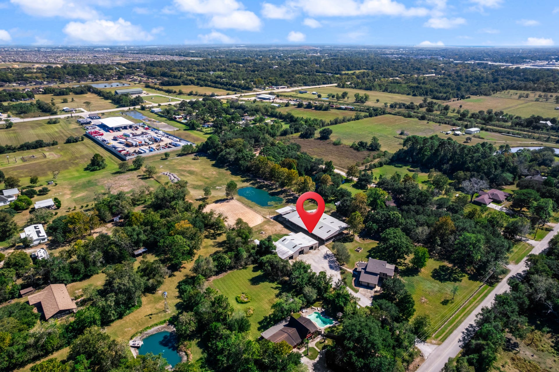 2215 Avenue Q, Santa Fe, TX 77510 Expansive aerial view showcasing this unique Santa Fe, Texas horse property, surrounded by mature trees, open green spaces, and scenic countryside. The property's equestrian facilities, sand riding arena, and pond are visible, along with the residence and convenient access to nearby roads. A wonderful combination of country living, equestrian amenities, and accessibility to surrounding communities.