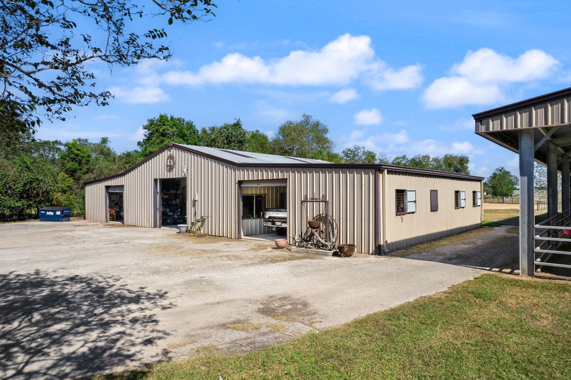 2215 Avenue Q, Santa Fe, TX 77510 Expansive metal workshop and equestrian building featuring multiple overhead roll-up doors, dedicated work and storage areas, and an adjoining horse barn. Generous gravel parking and maneuvering space provide convenient access for vehicles, trailers, and equipment.