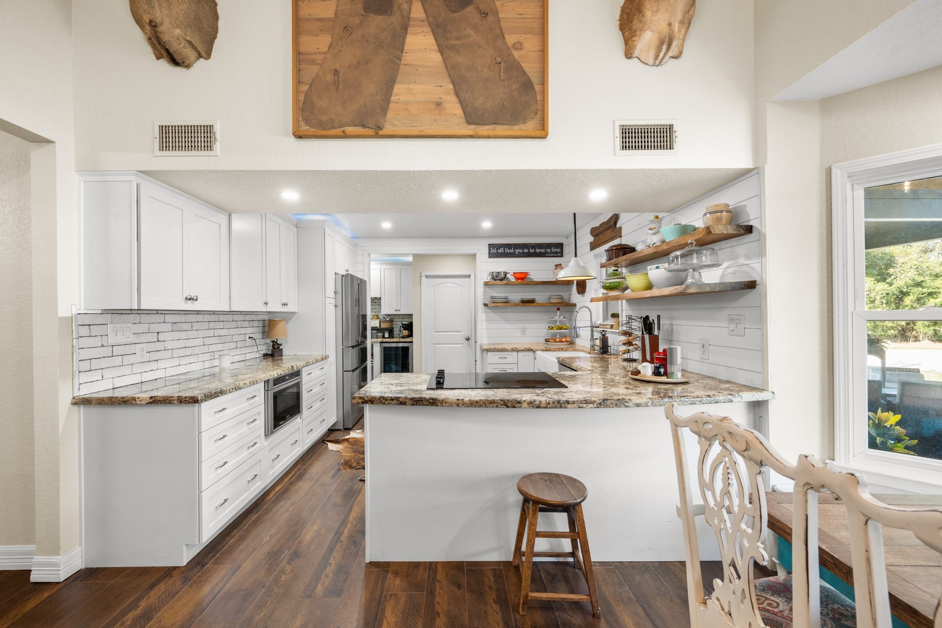 2215 Avenue Q, Santa Fe, TX 77510 Farmhouse charm meets modern convenience with granite countertops, crisp white cabinetry, floating wood shelves, and a generous breakfast bar with an electric cooktop.