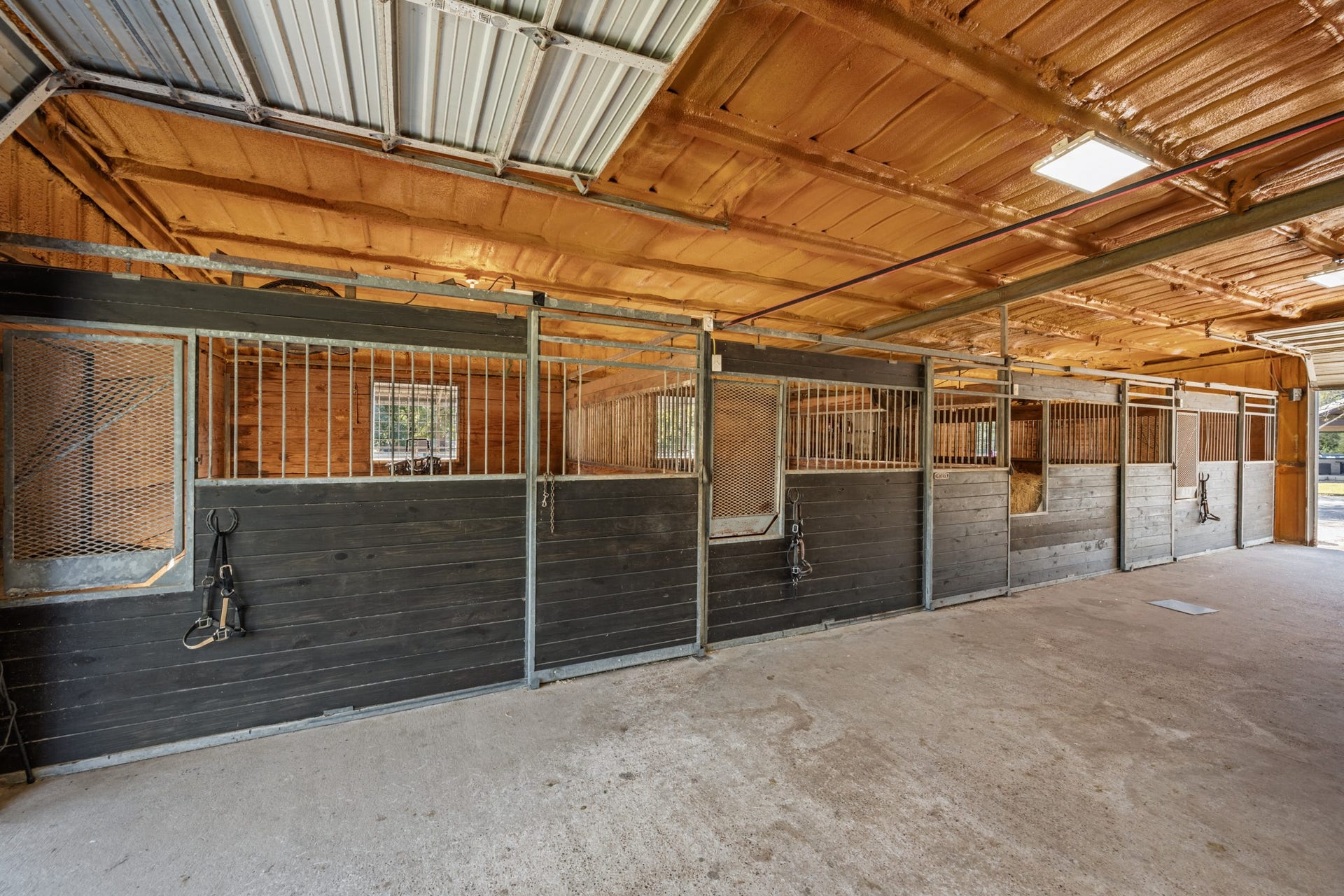 2215 Avenue Q, Santa Fe, TX 77510 Well-appointed equestrian barn featuring multiple horse stalls with sturdy wood-and-metal construction, a wide concrete center aisle, overhead lighting, and convenient exterior access.
