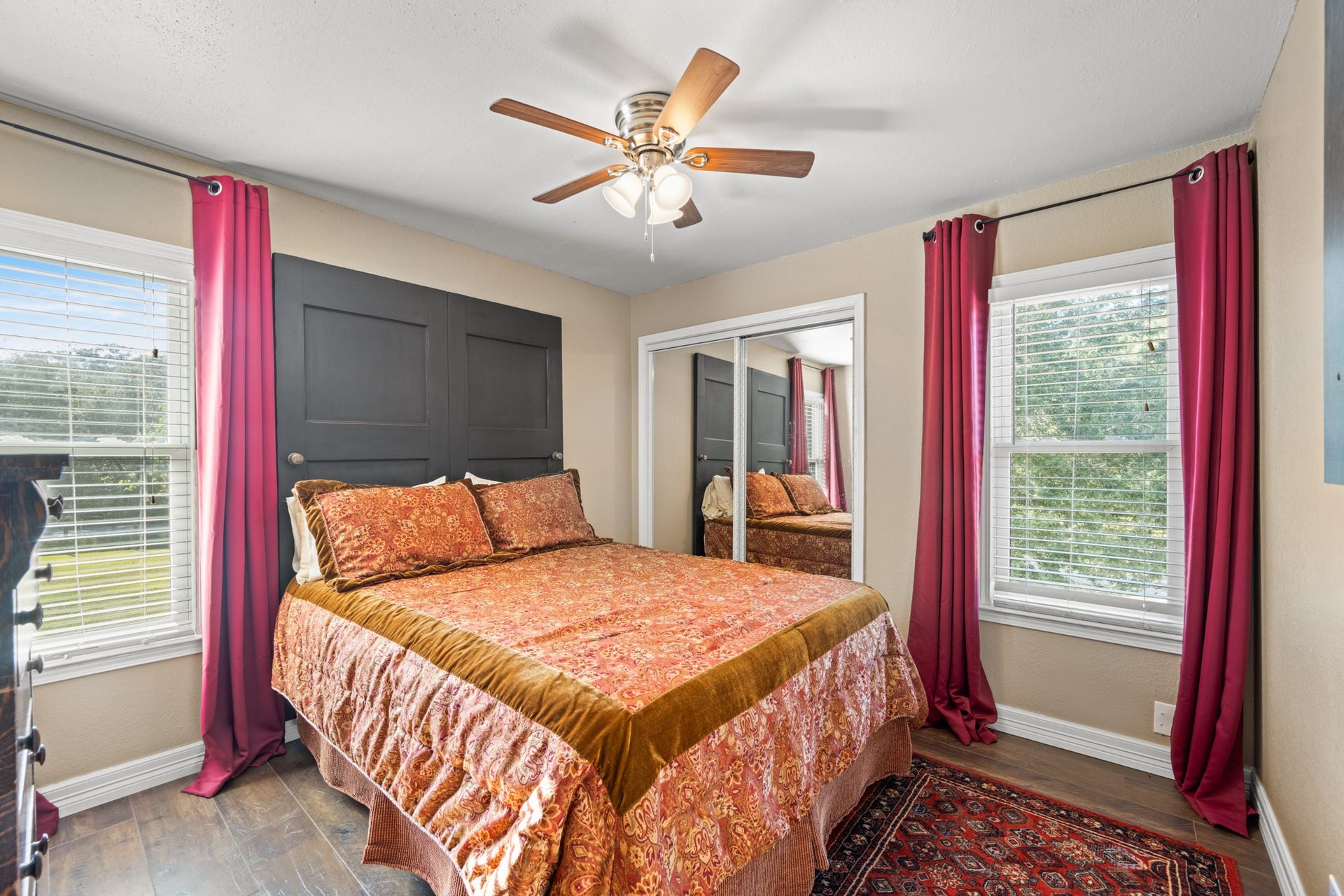 2215 Avenue Q, Santa Fe, TX 77510 Bright secondary bedroom features windows on two walls, mirrored closet doors, wood-look flooring, and a ceiling fan, creating a comfortable and functional retreat.