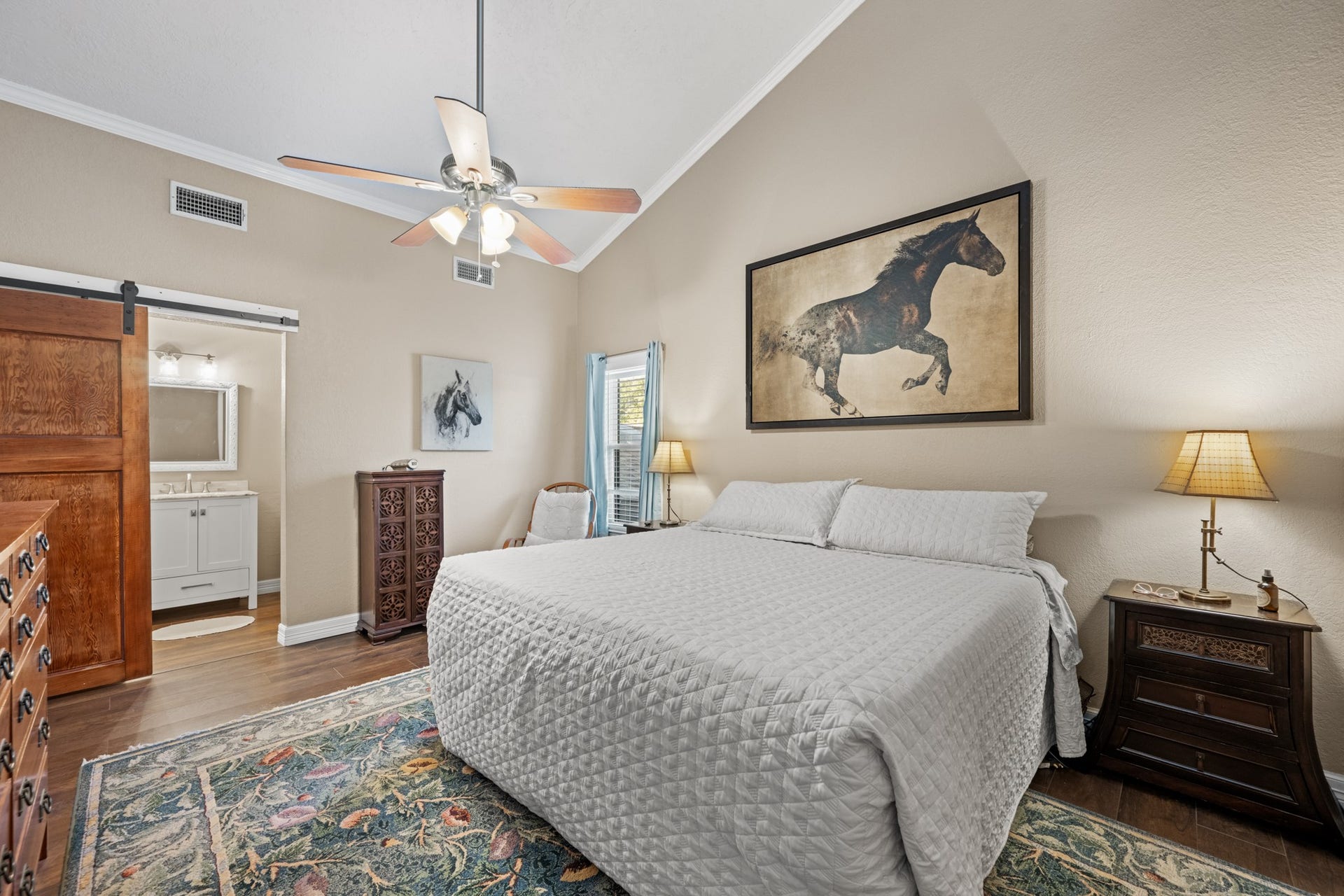 2215 Avenue Q, Santa Fe, TX 77510 Spacious primary suite features a vaulted ceiling, warm wood-look flooring, ceiling fan, and a rustic sliding barn door leading to the ensuite bathroom.