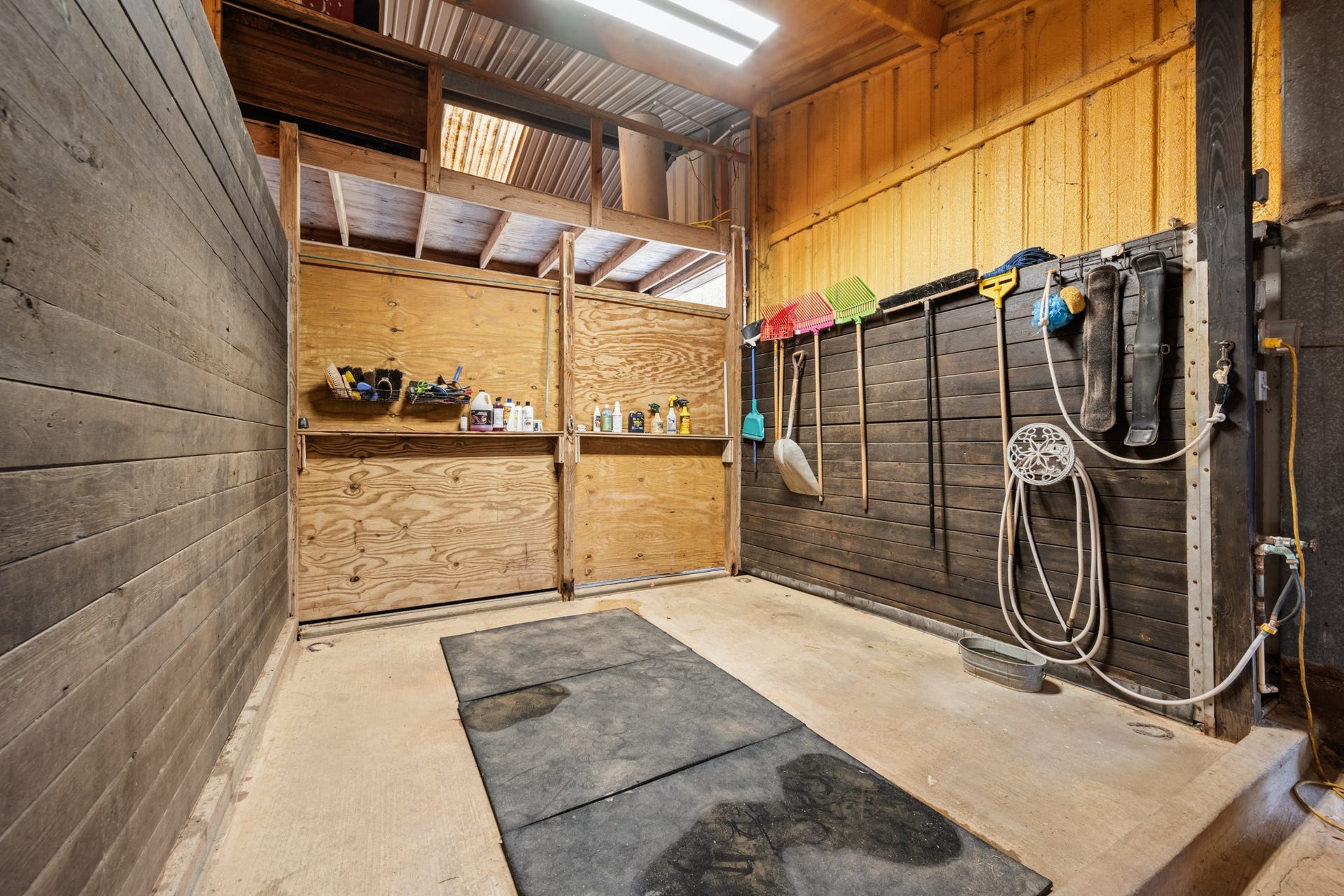 2215 Avenue Q, Santa Fe, TX 77510 Dedicated horse wash and grooming bay featuring rubber floor mats, wood-paneled walls, water access, and convenient storage for grooming essentials.